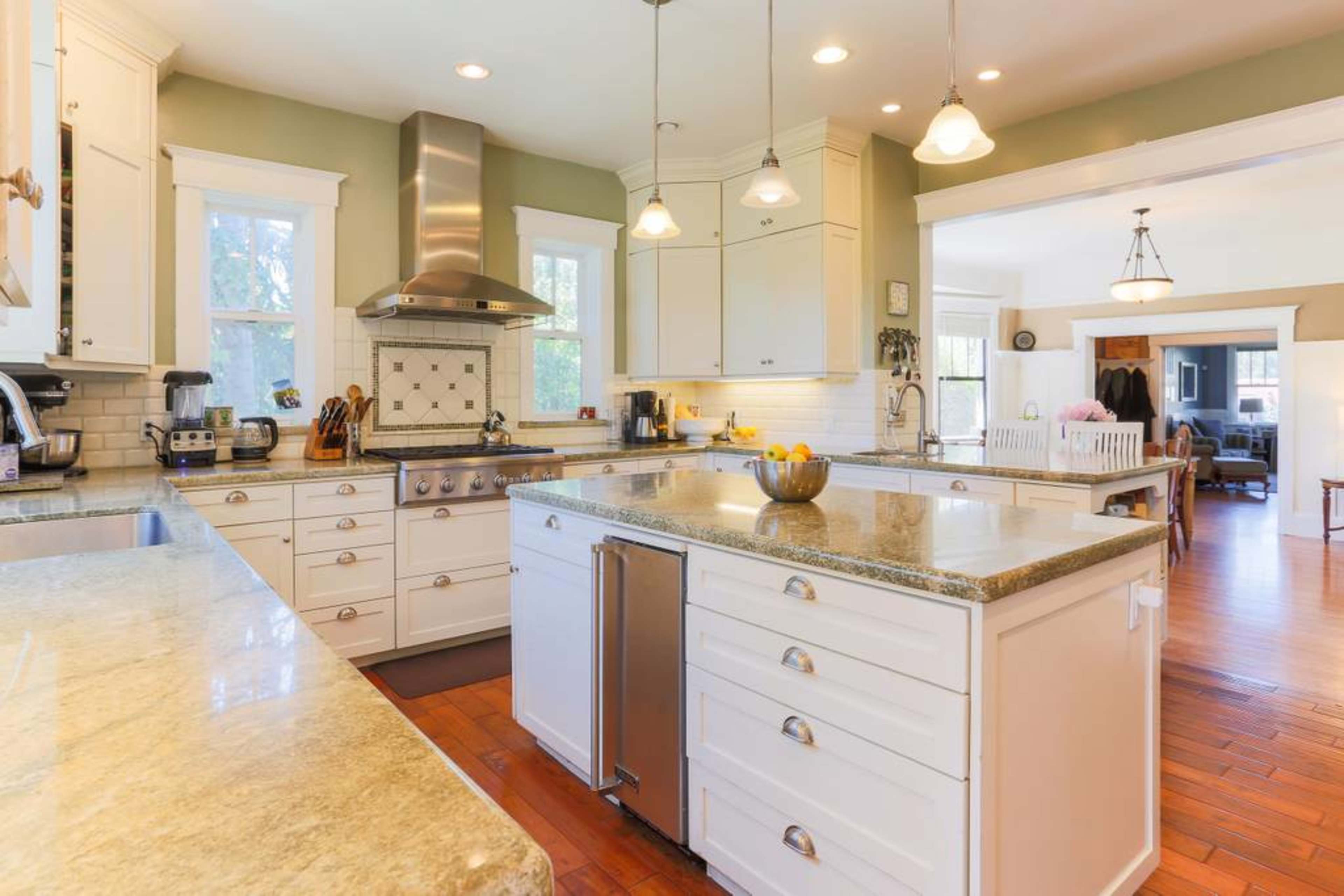 A spacious kitchen features white cabinetry, a large island with a granite countertop, stainless steel appliances, and hardwood floors.