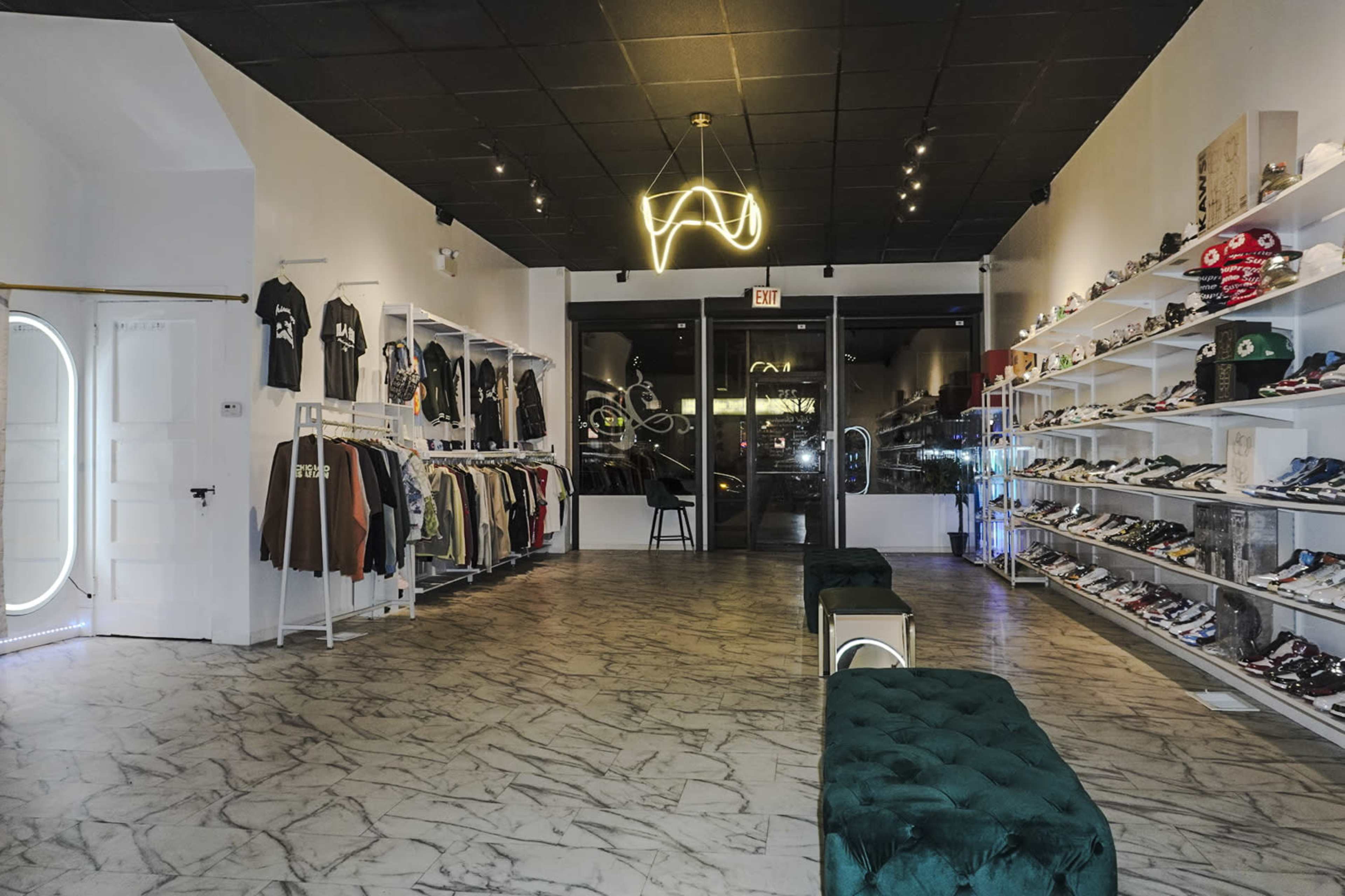 The interior of a retail store features clothing racks on the left and shelves displaying sneakers on the right, with a modern lighting fixture overhead.