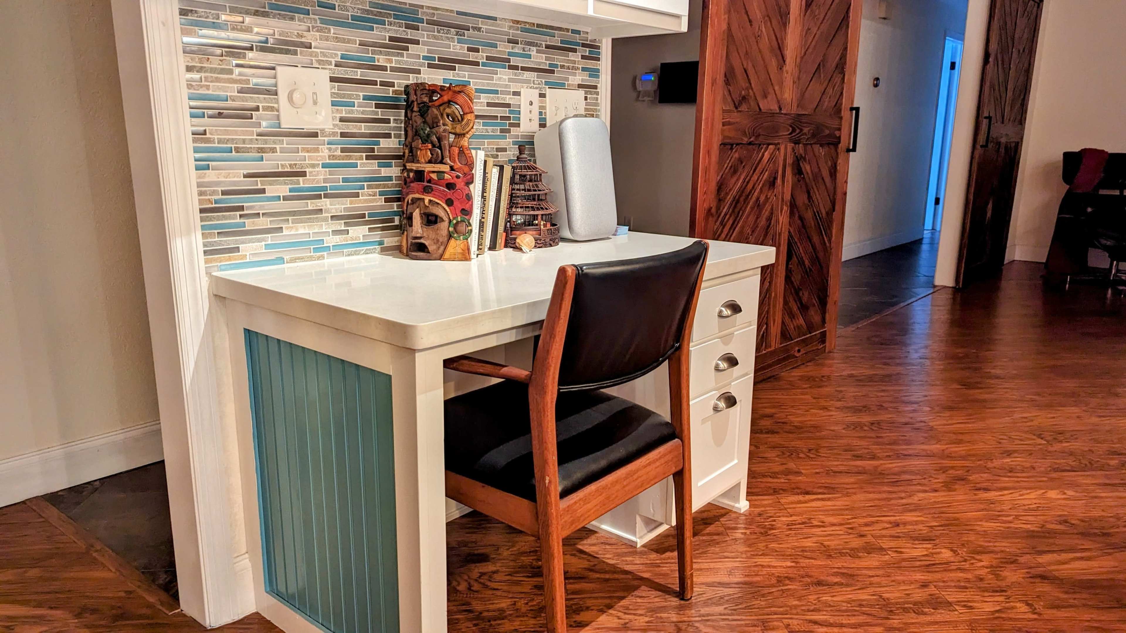 A small desk with a black chair is positioned against a wall featuring a decorative backsplash of blue and gray tiles.