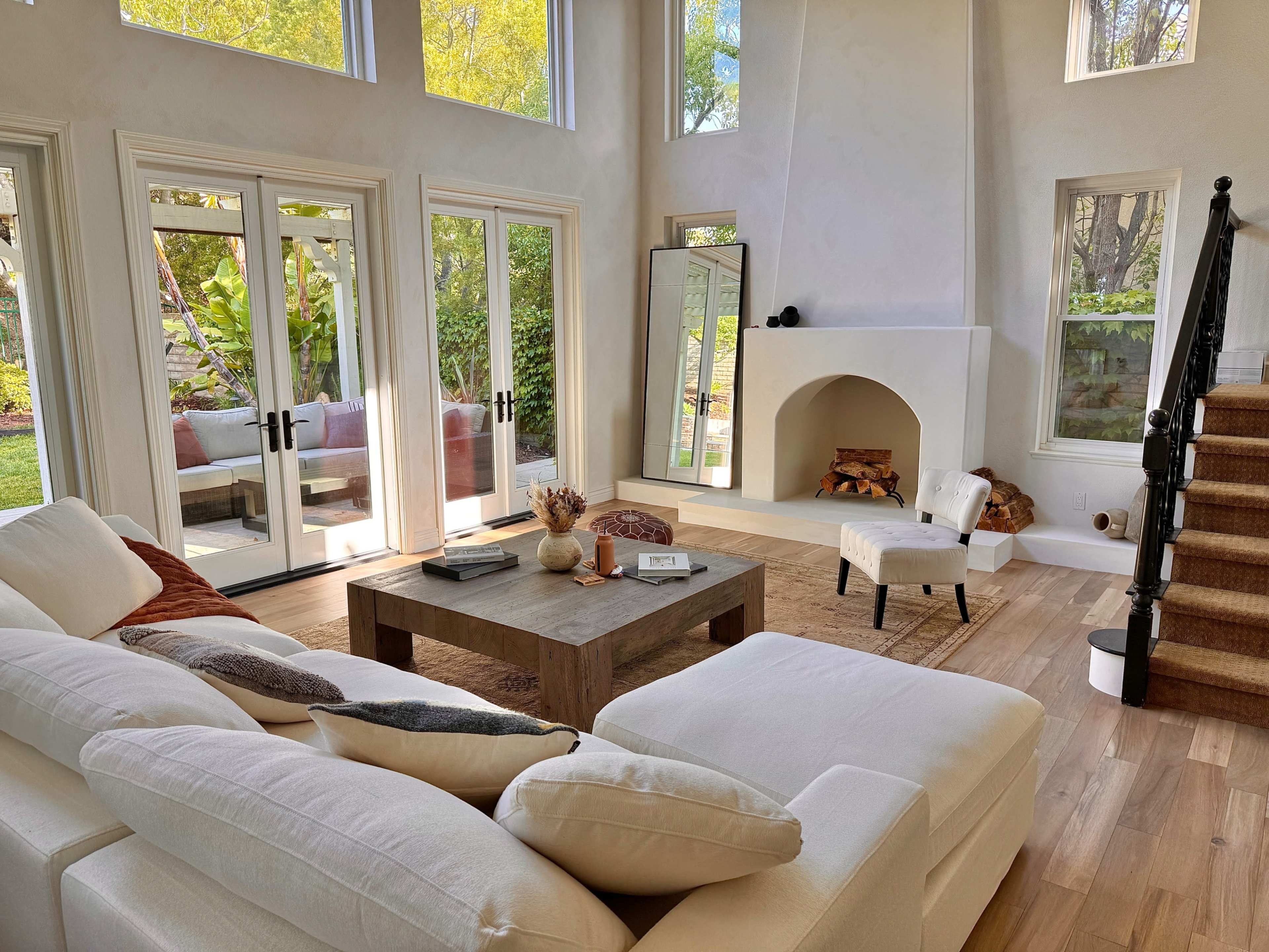 A modern, bright living room featuring a large white sectional sofa, a wooden coffee table, and a fireplace, with sliding glass doors opening to an outdoor space.