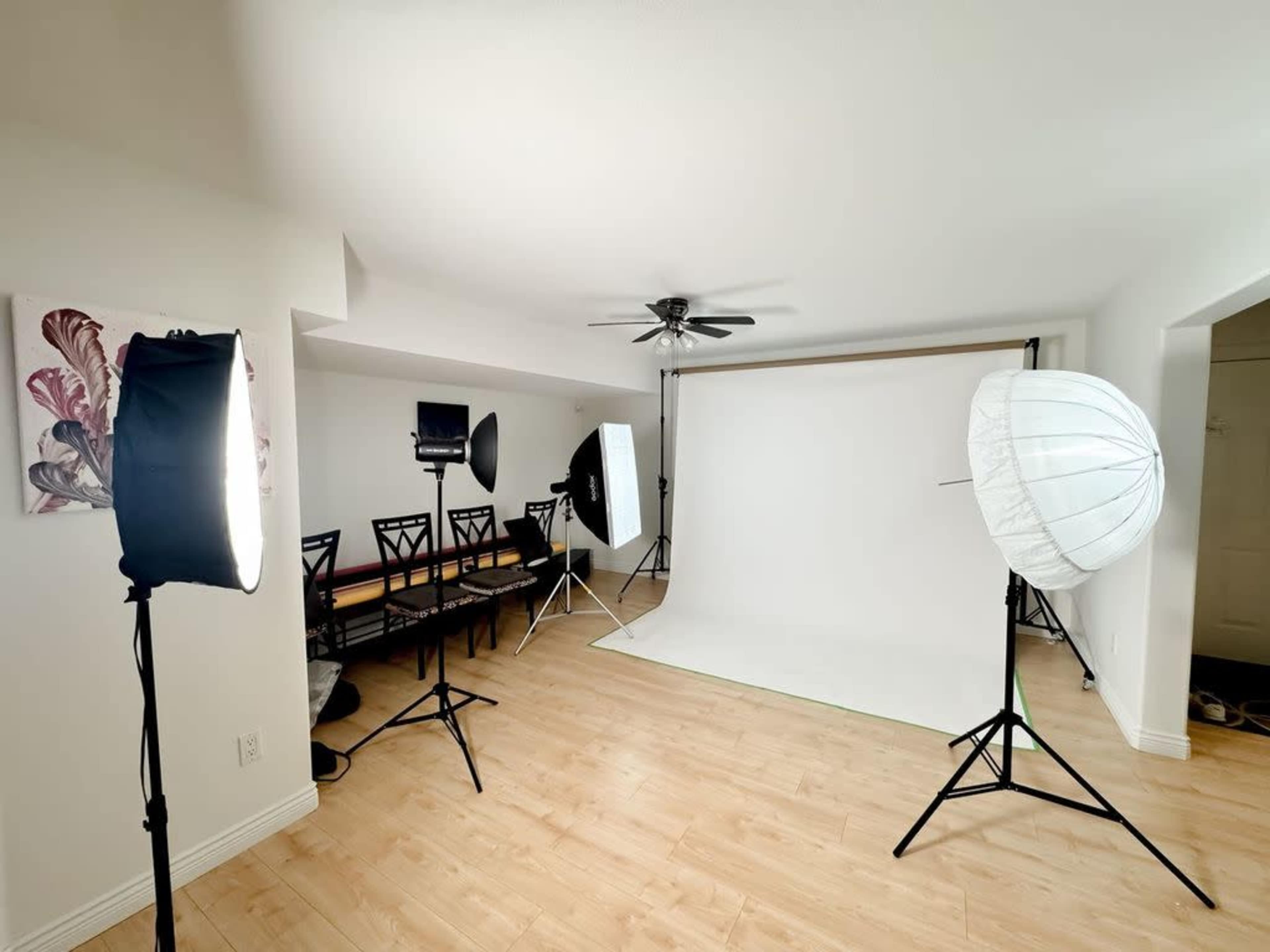The image shows a photography studio setup with various lighting equipment and a white backdrop in a spacious room.
