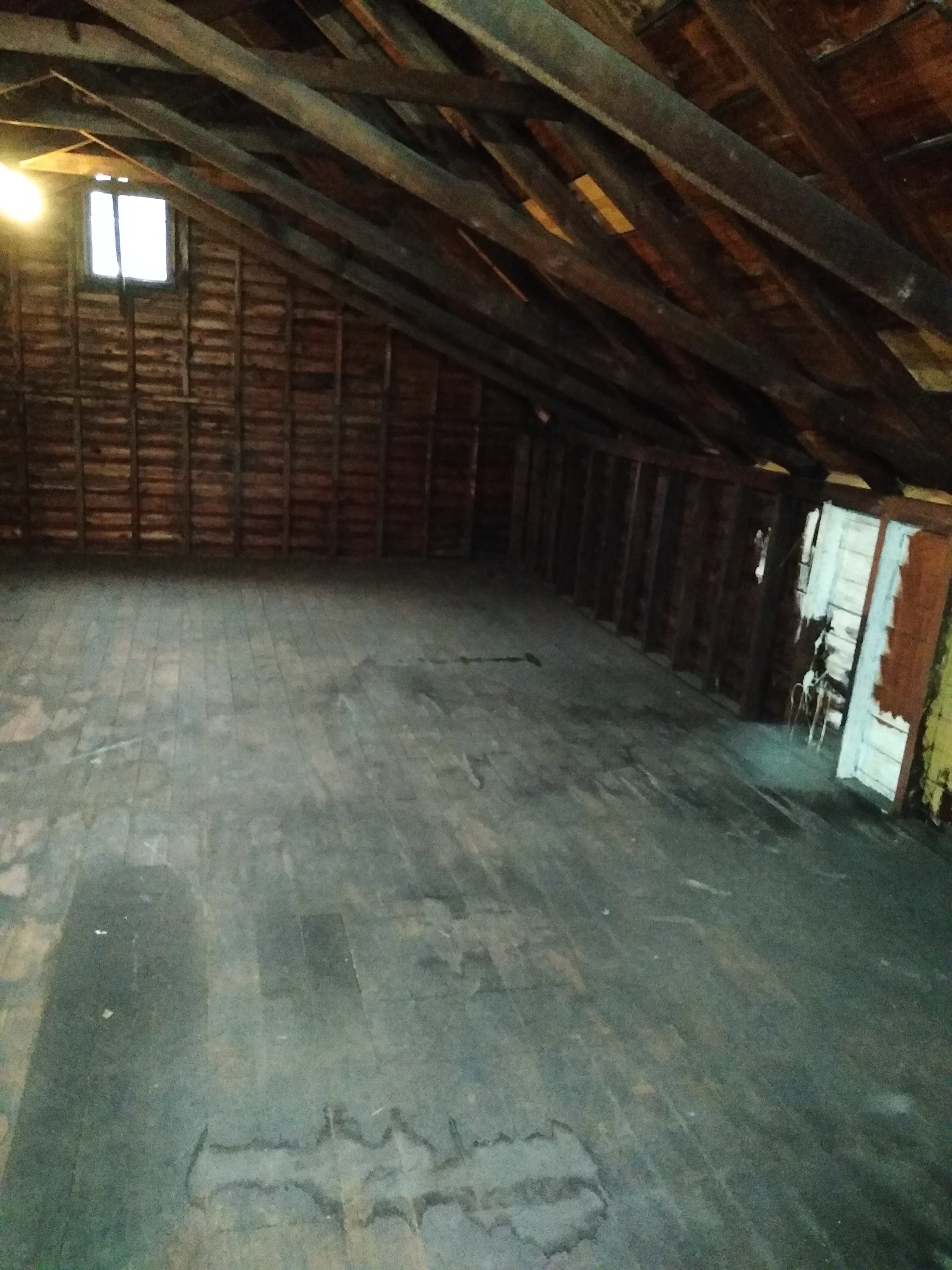 A spacious, empty attic with exposed wooden beams and planks.