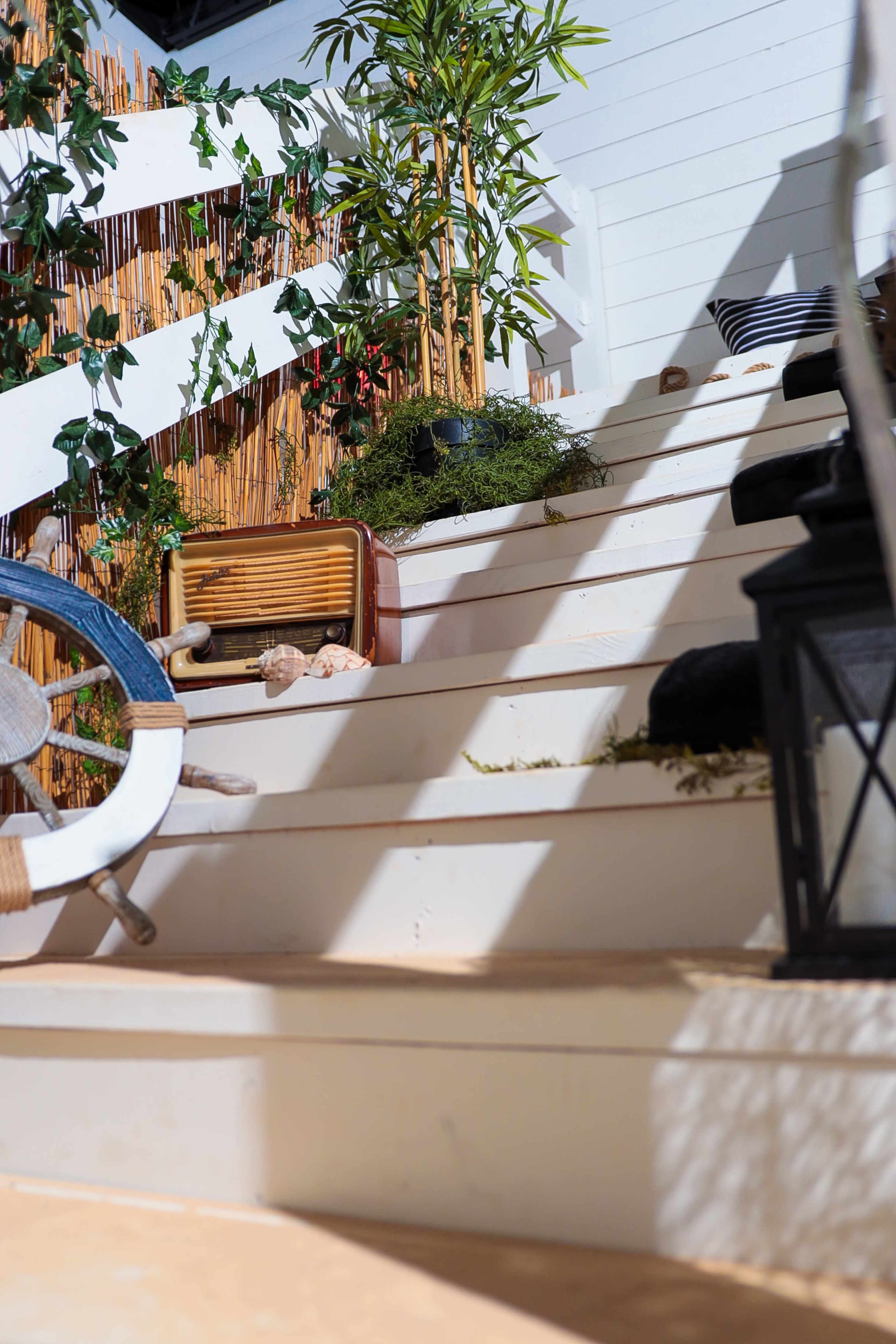 The image shows a wooden staircase adorned with decorative items, greenery, and scattered objects.
