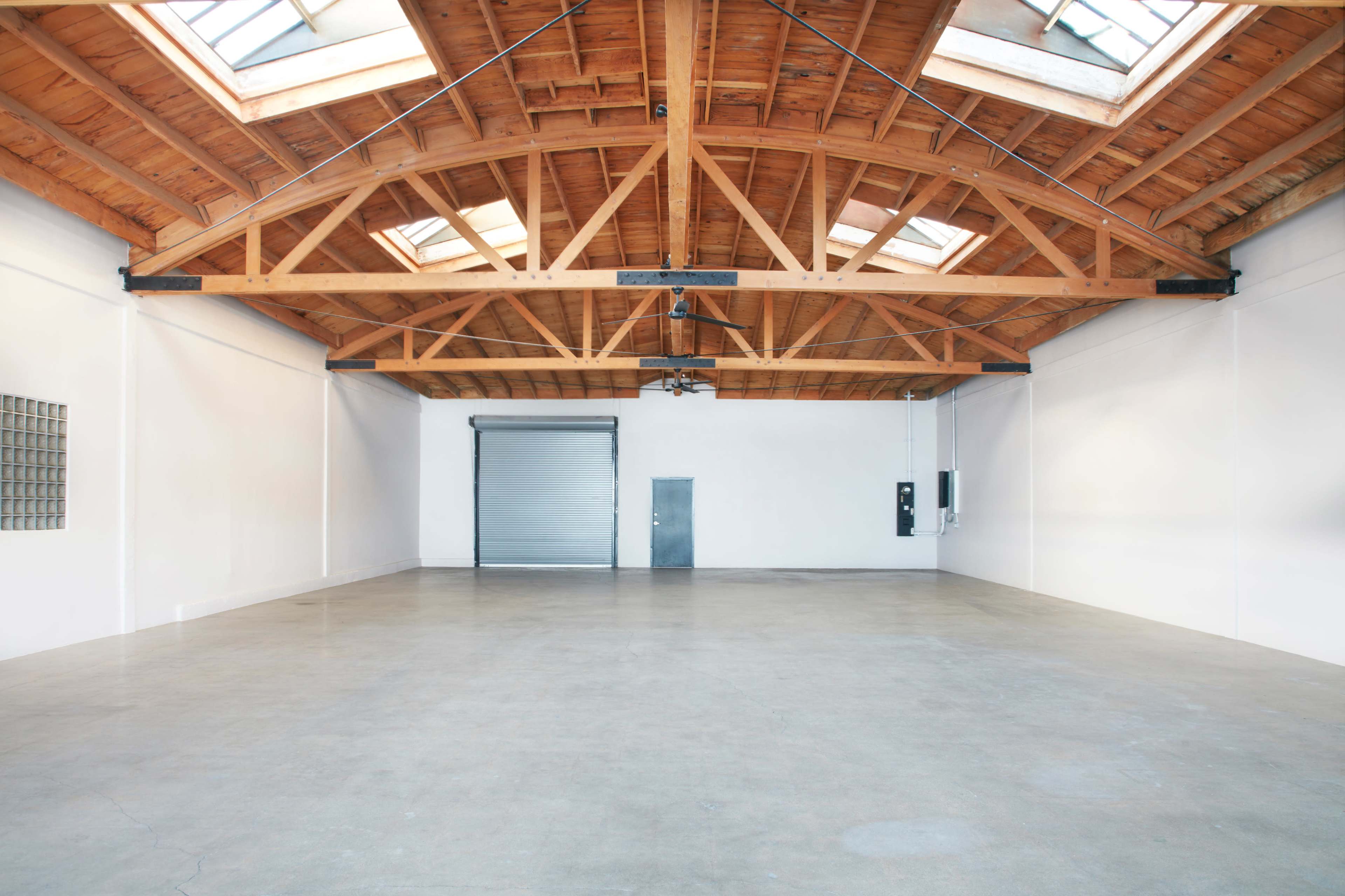 An empty industrial space with a wooden beam ceiling, large windows, and a gray door.
