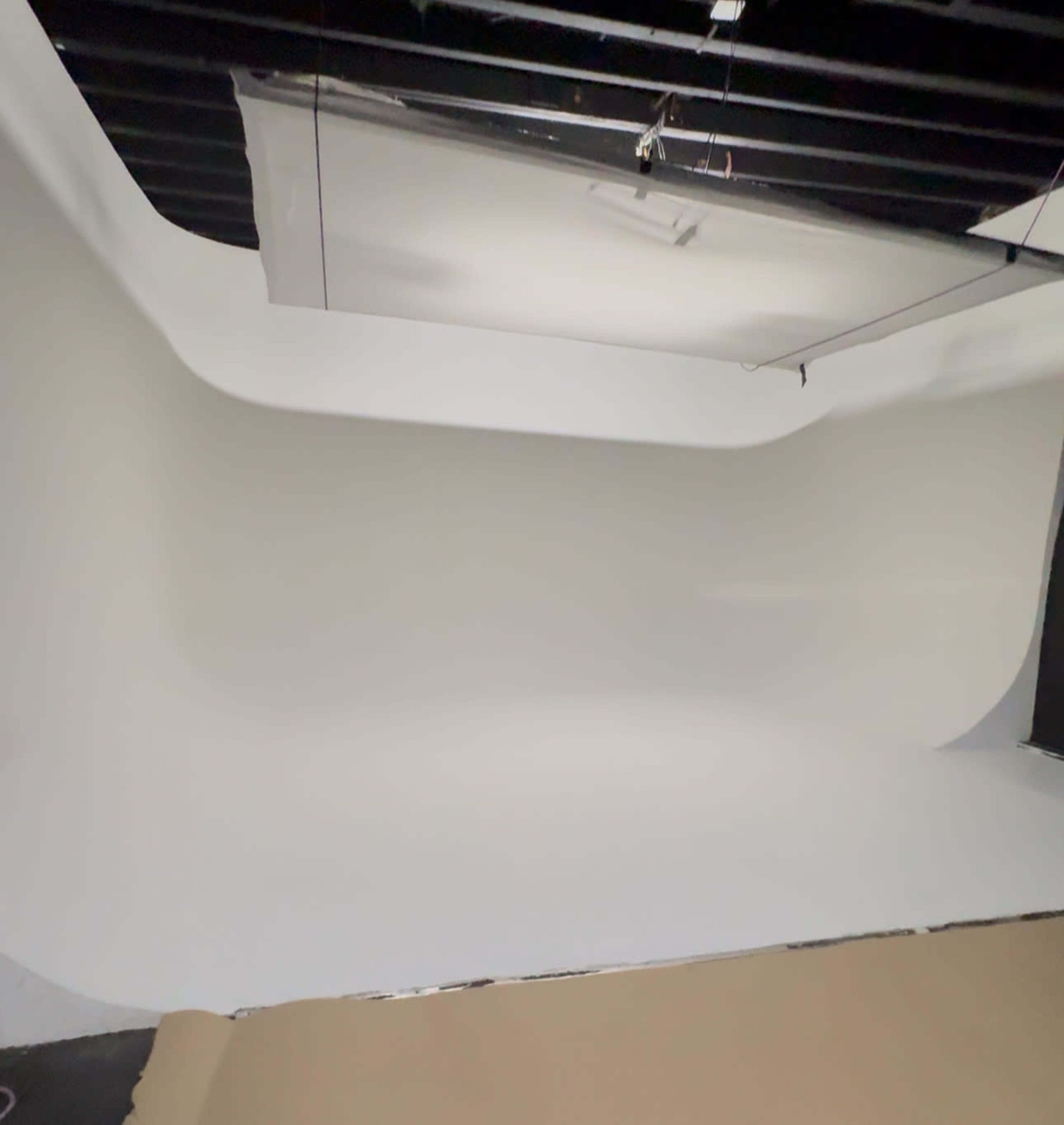 The image shows a spacious photography studio with a seamless white backdrop and a softbox light hanging from the ceiling.