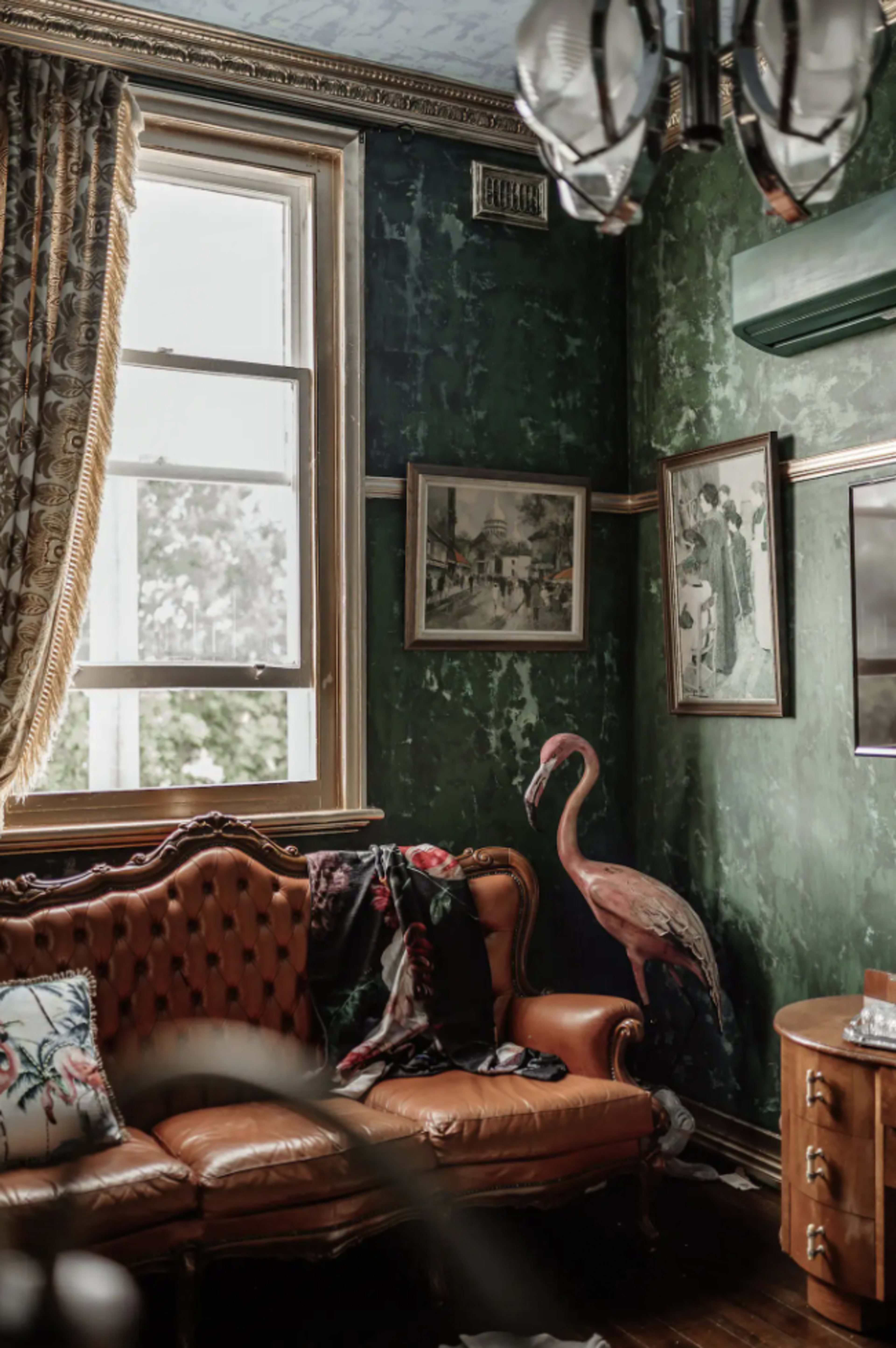 The image features a vintage living room with a green textured wall, a framed artwork, a brown leather sofa, and a pink flamingo decoration in the corner.