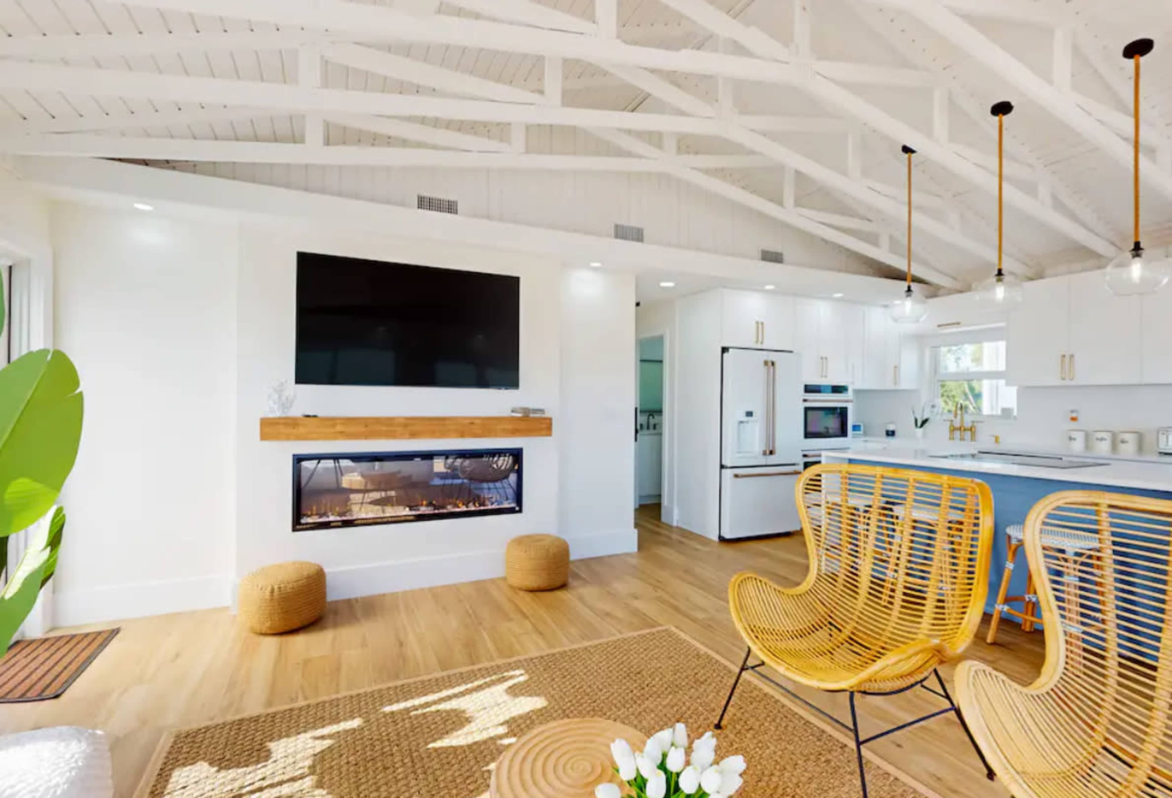 A modern living space featuring a fireplace, large television, and open kitchen area with wooden flooring and decorative furniture.