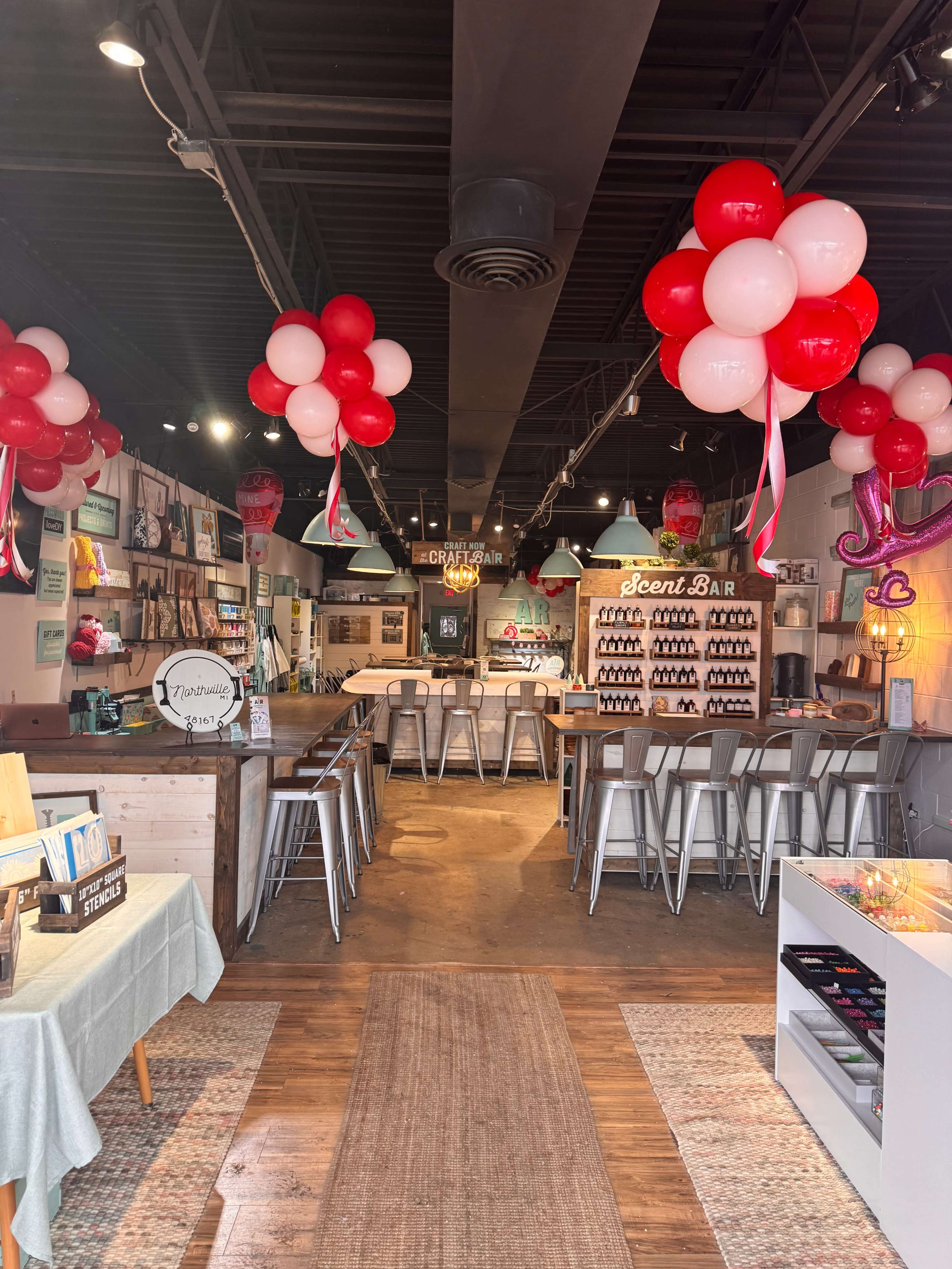 The image shows a boutique shop interior decorated with red and white balloons, featuring a scent bar, seating area, and various merchandise displays.