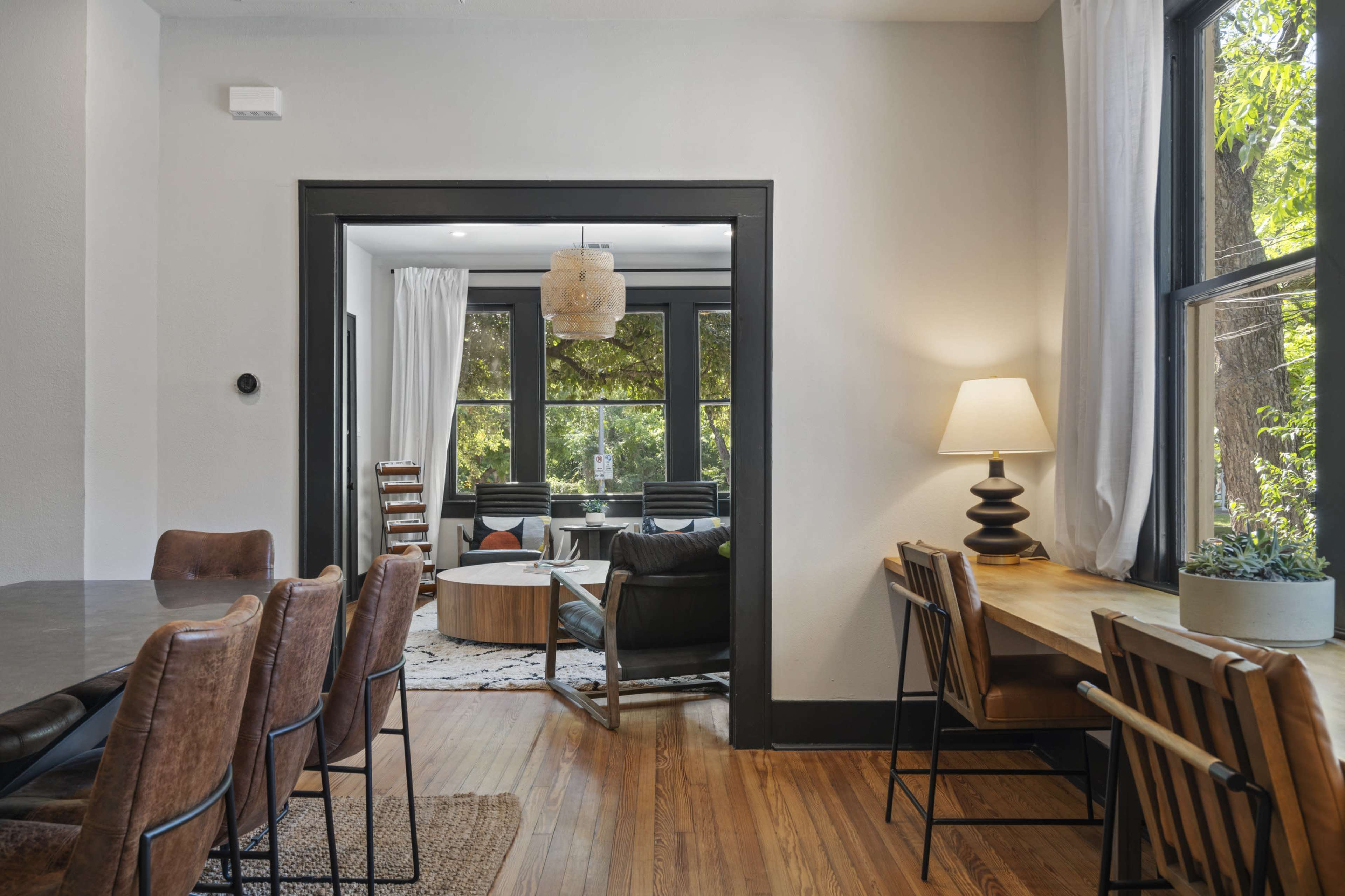 A spacious living area with a dining table and chairs on one side, and a cozy sitting area with large windows on the other.