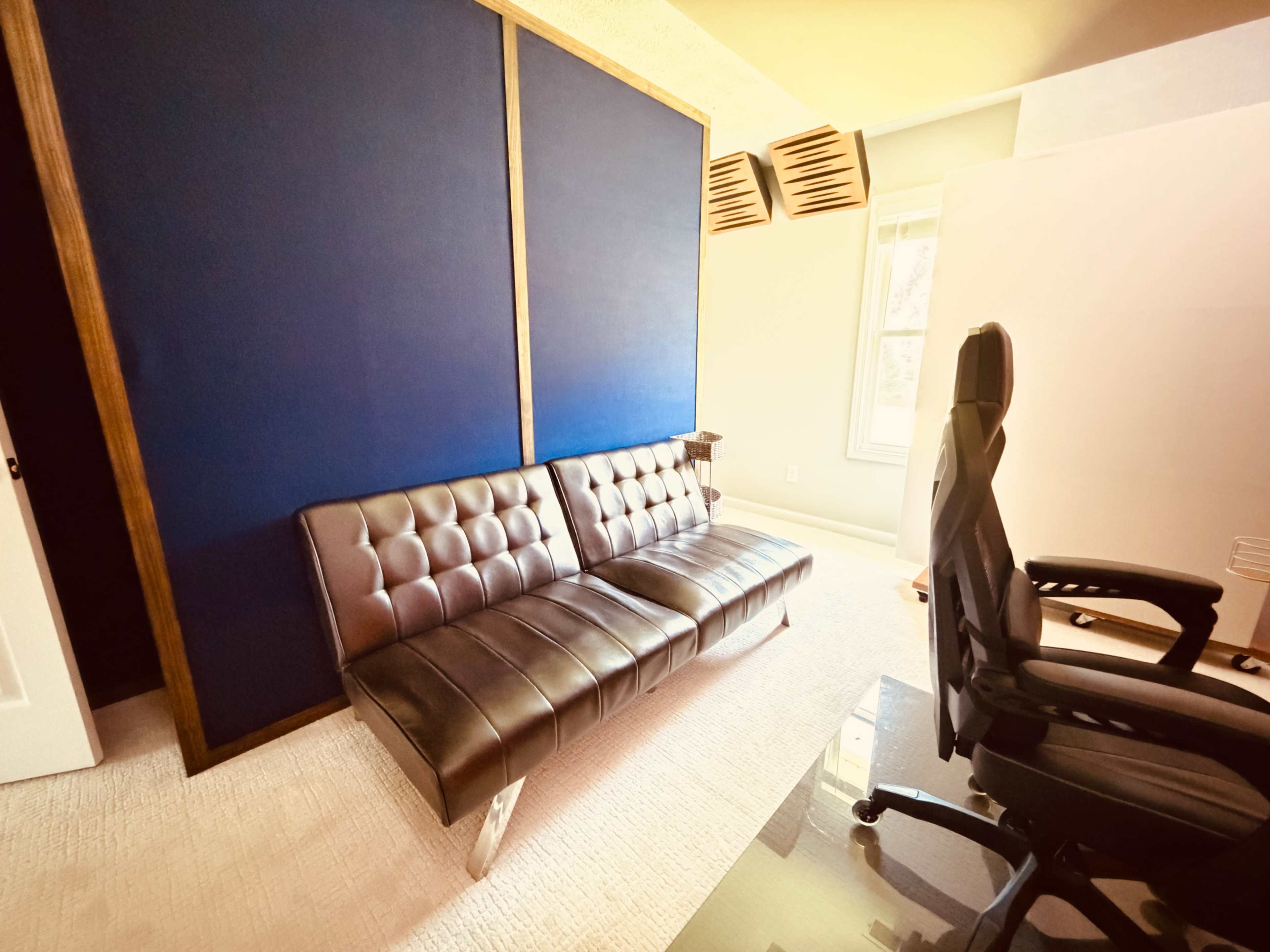 The image shows a modern office space with a brown tufted sofa, a black ergonomic chair, and a blue wall partition.