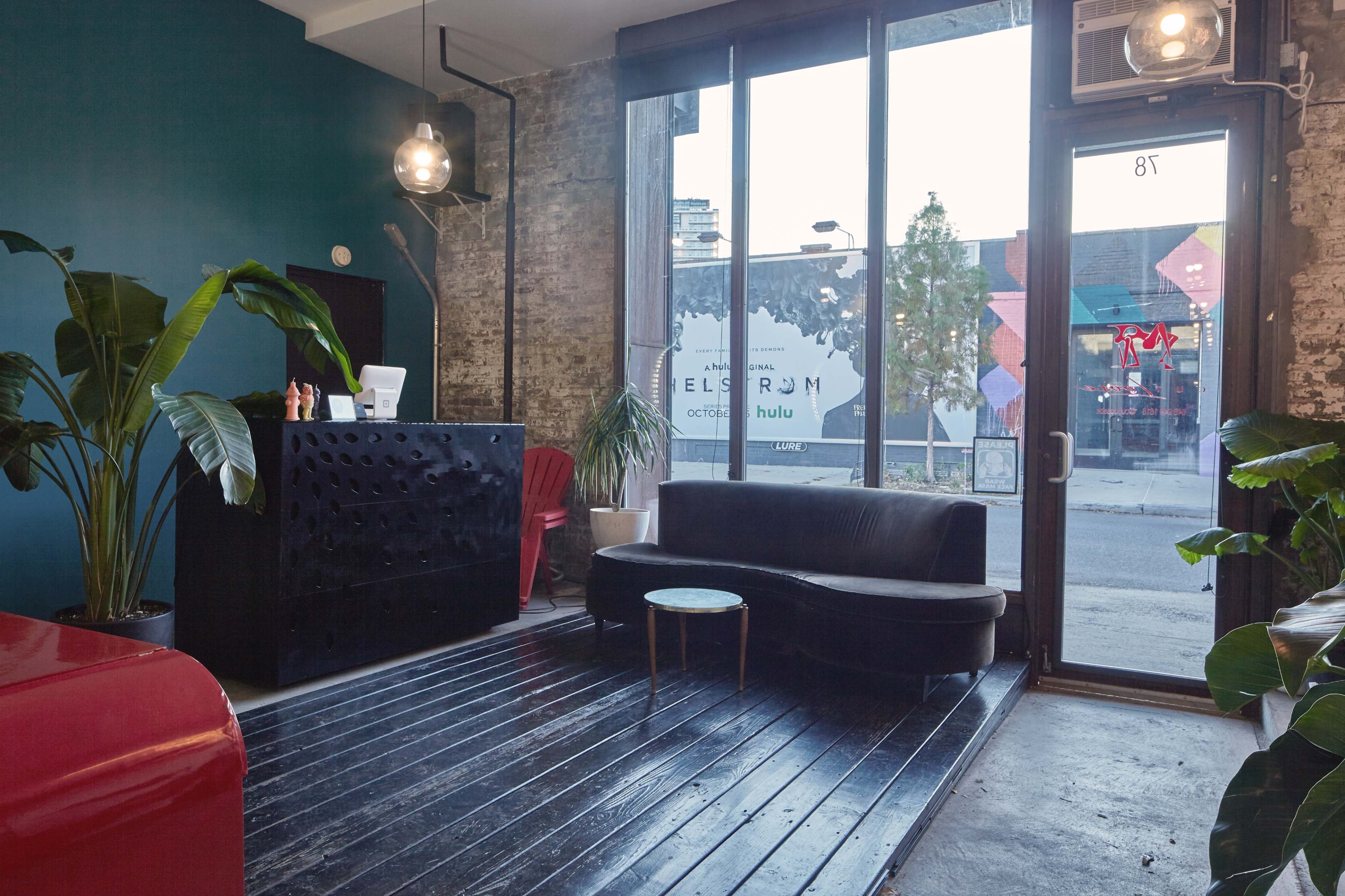 A modern reception area with a black couch, a coffee table, and large windows displaying a street view.