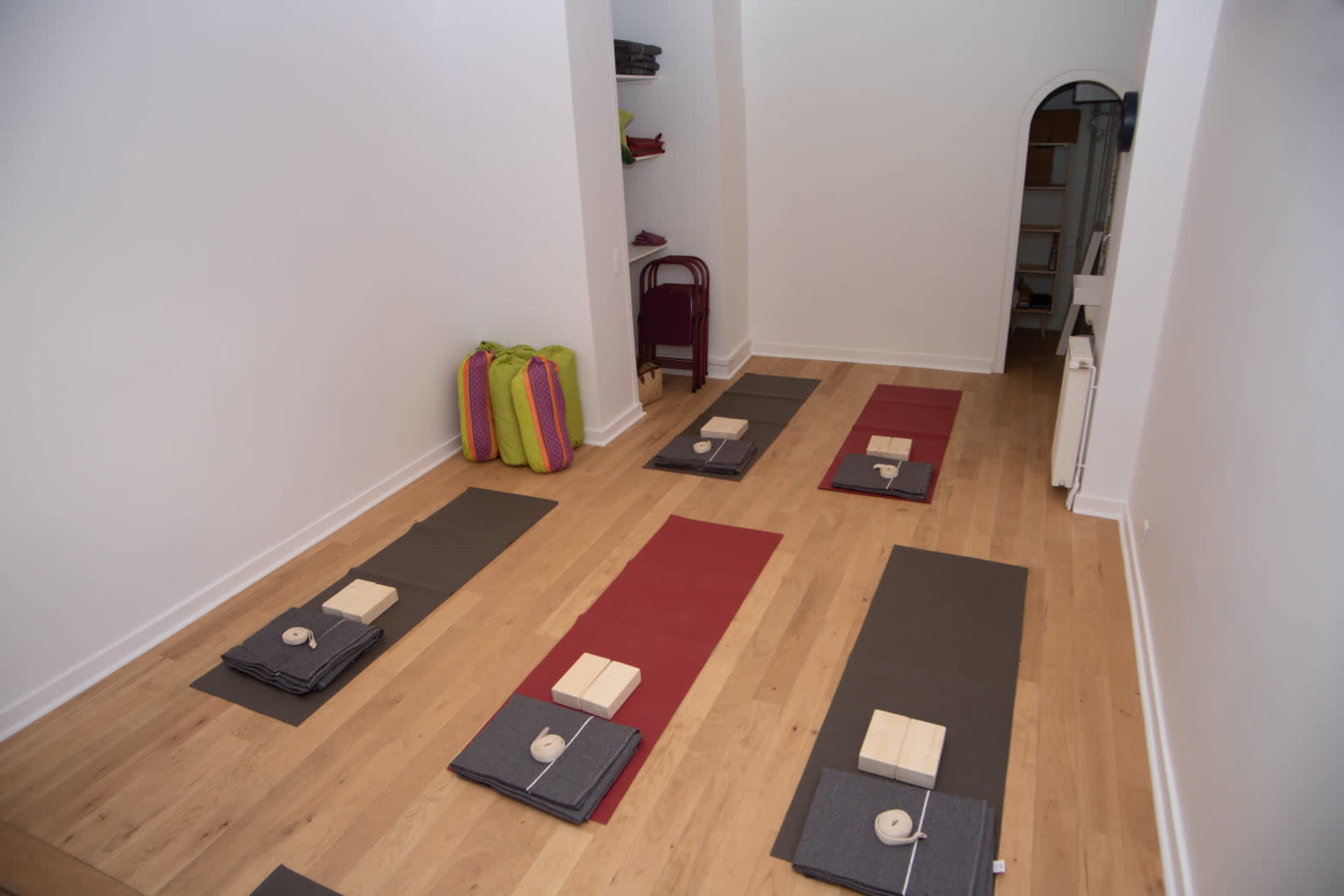 A serene yoga studio with several yoga mats laid out on a wooden floor, each equipped with blocks and straps, and neatly organized on shelves in the background.