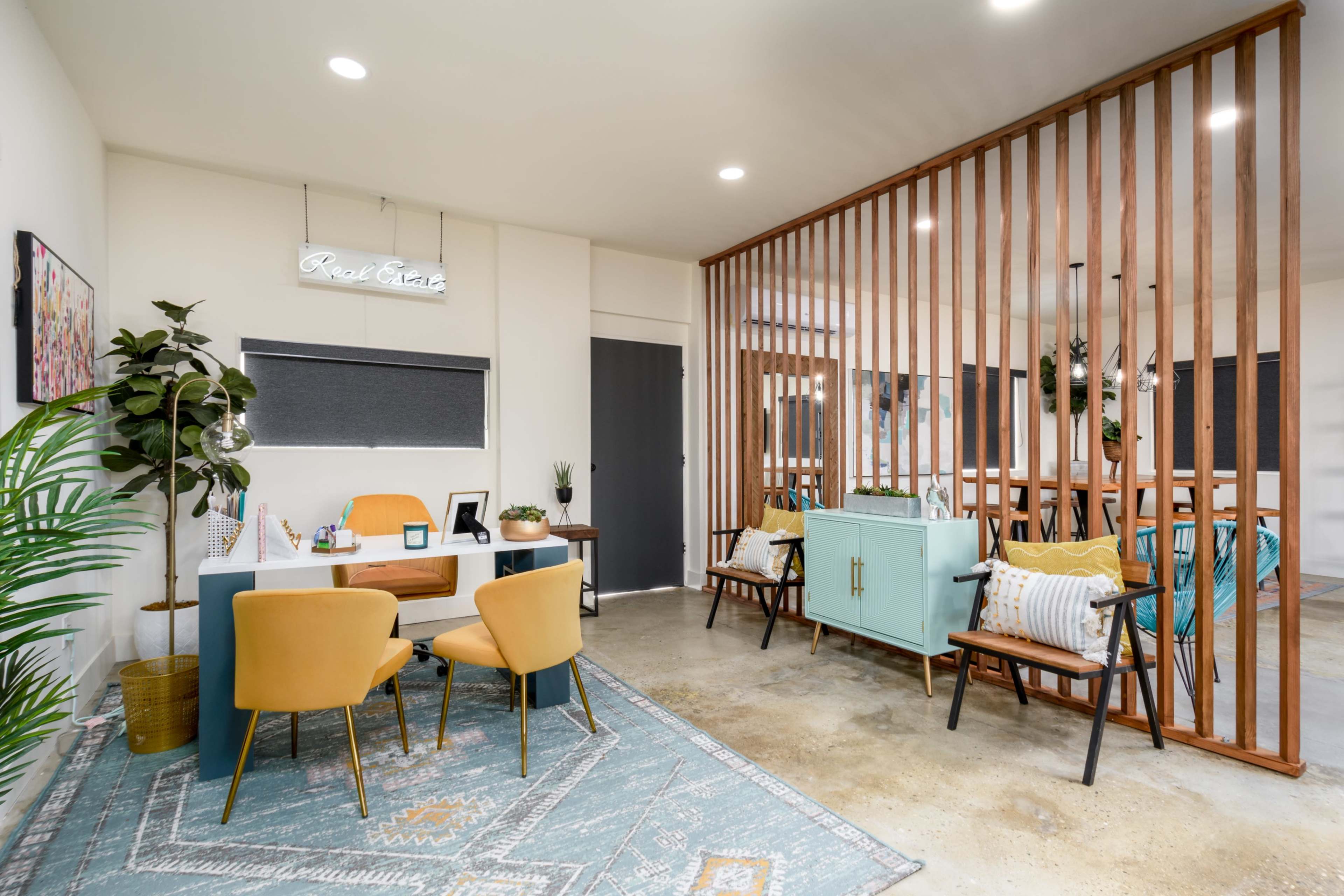 A modern office interior features a desk with yellow chairs, a decorative plant, and a wooden partition separating a seating area with teal furniture.