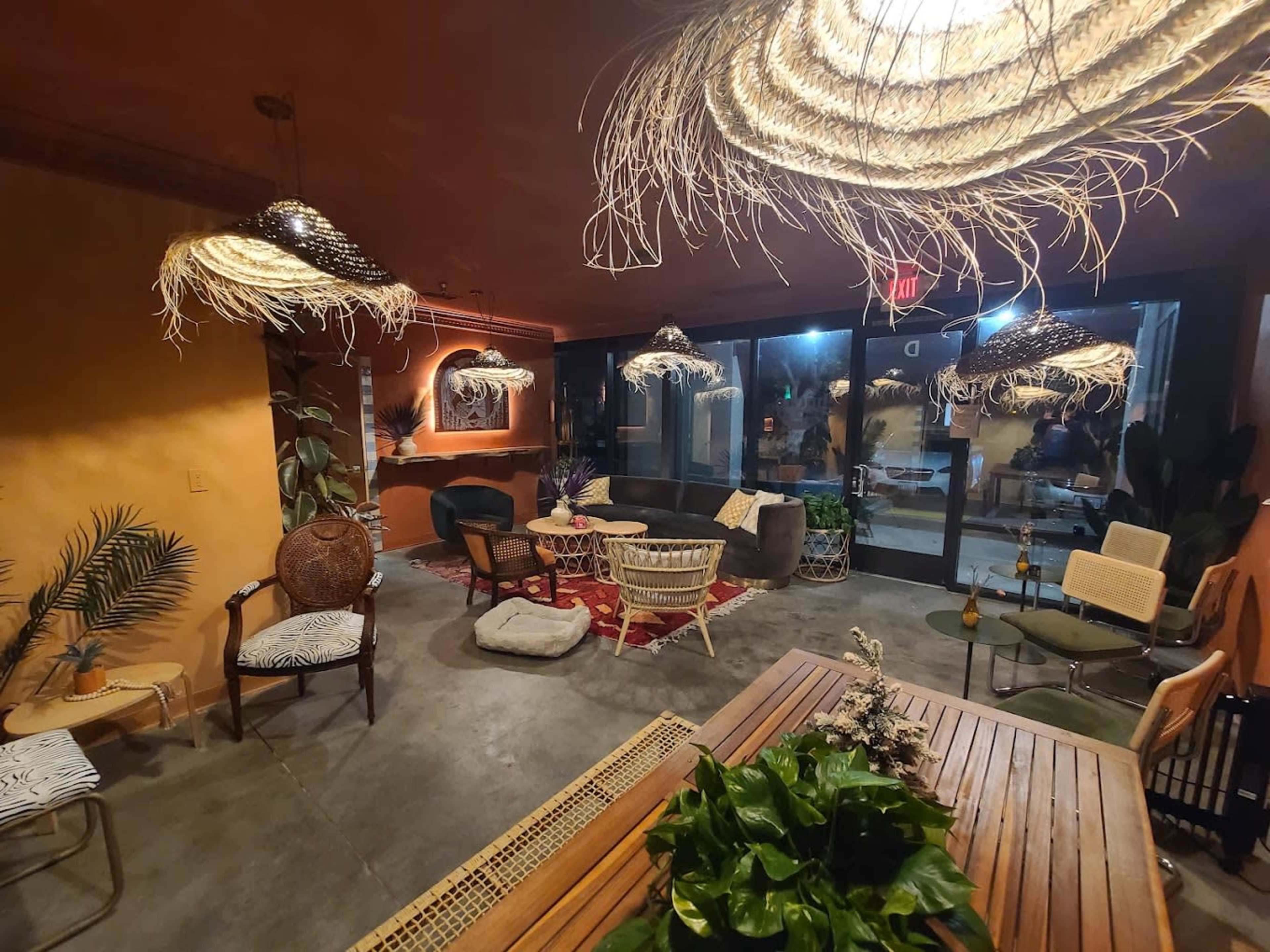 A cozy indoor lounge area with various seating arrangements, decorative plants, and unique woven light fixtures.