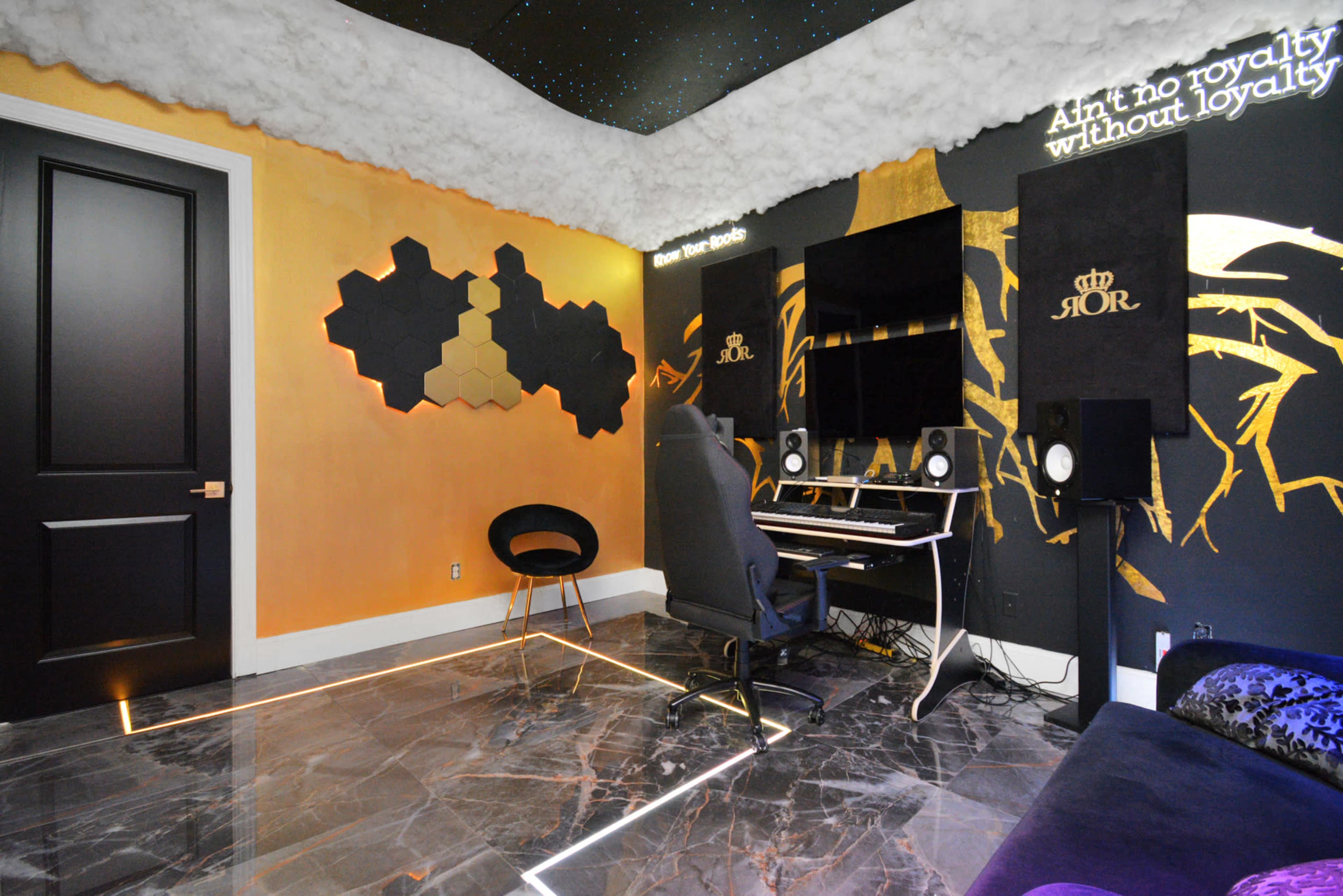 The image shows a modern music studio with a keyboard, speakers, and a wall decorated with geometric shapes and inspirational text under a cloud-like ceiling.