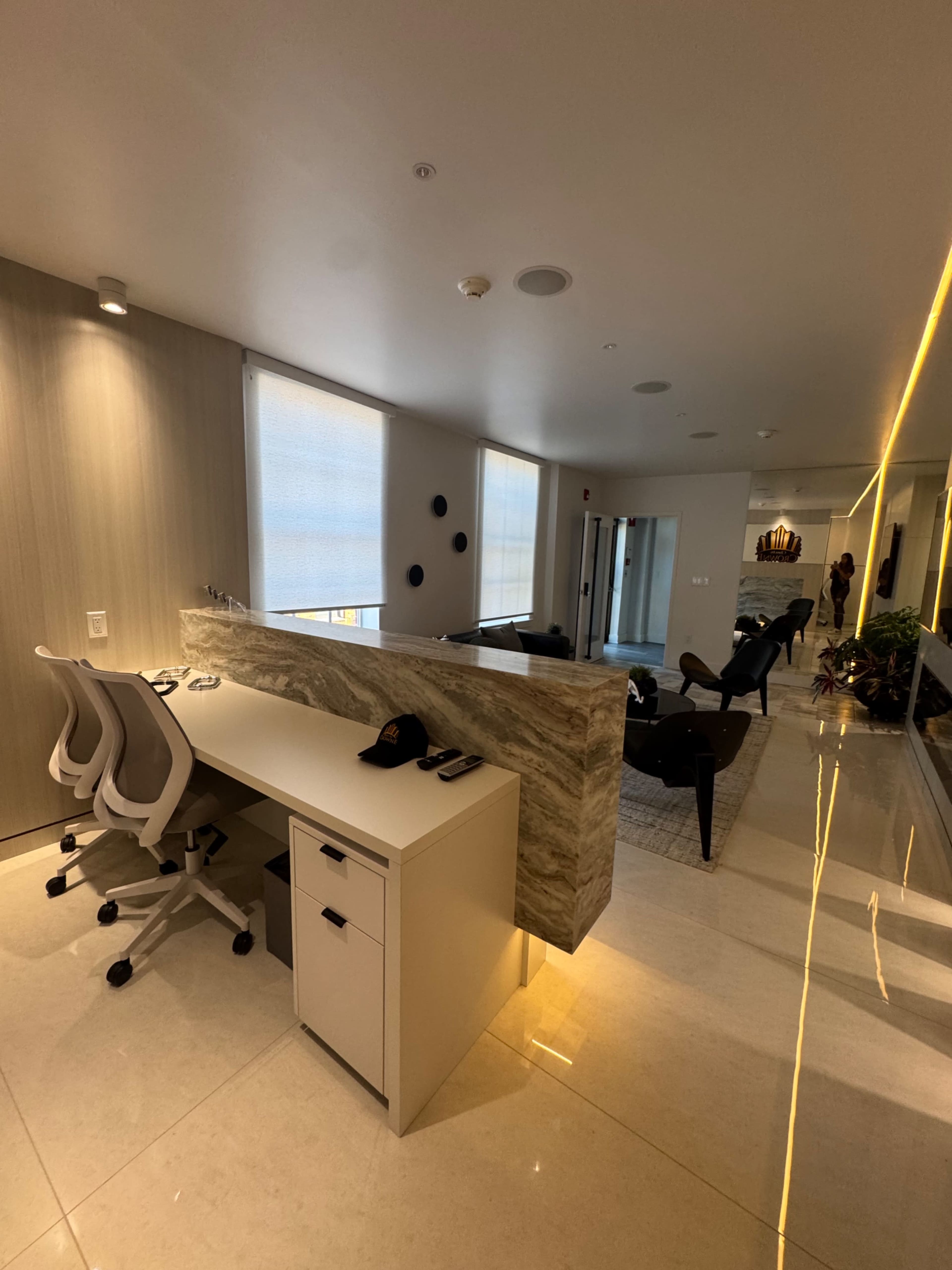 The image shows a modern office space with a sleek desk, two office chairs, and a stone reception area, illuminated by soft lighting.