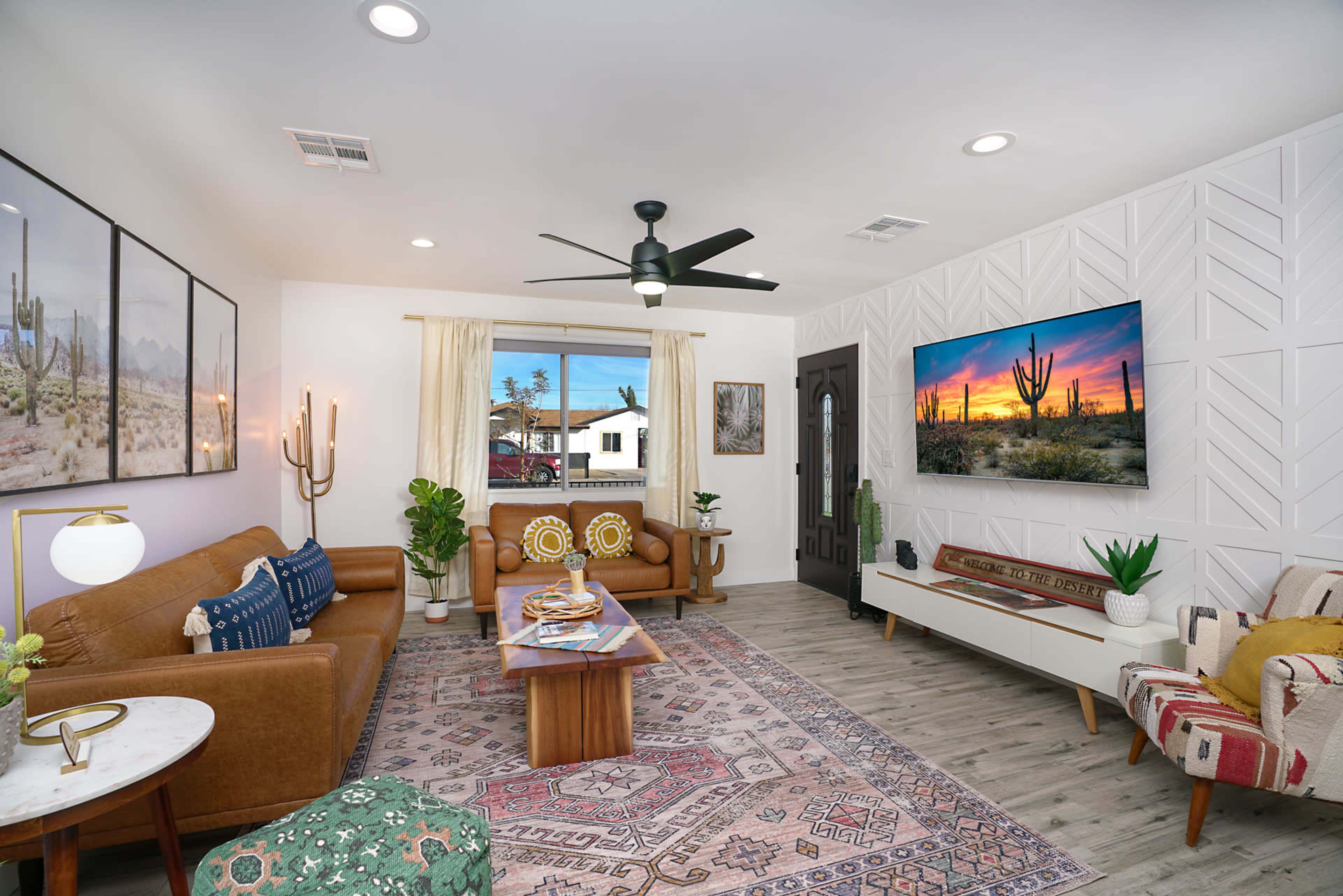 A living room features brown leather sofas, a wooden coffee table, a decorative rug, and a wall-mounted television displaying a desert landscape.