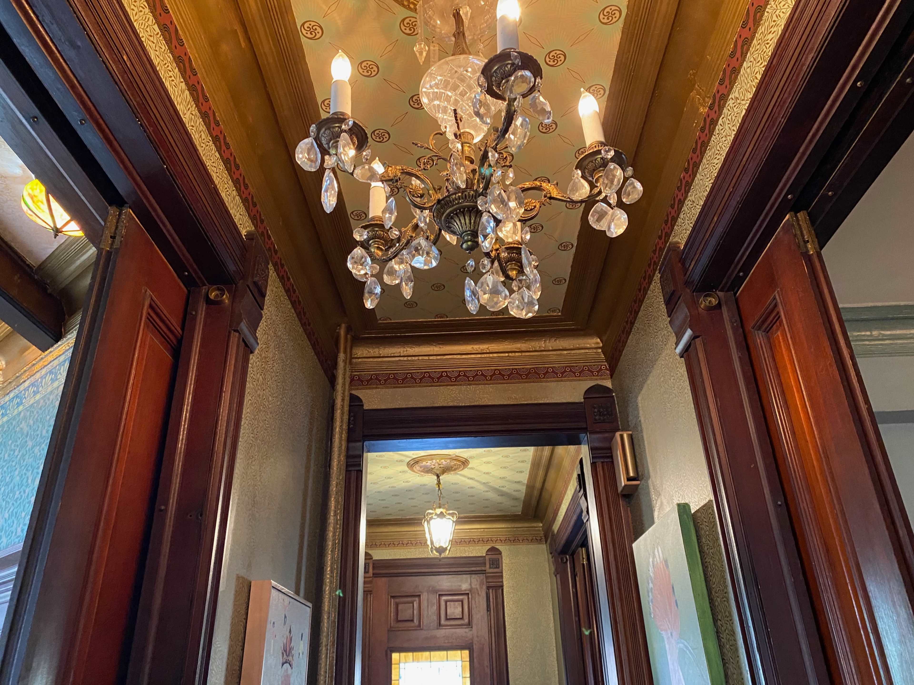 A vintage hallway with wooden doors and a decorative chandelier hanging from the ceiling.