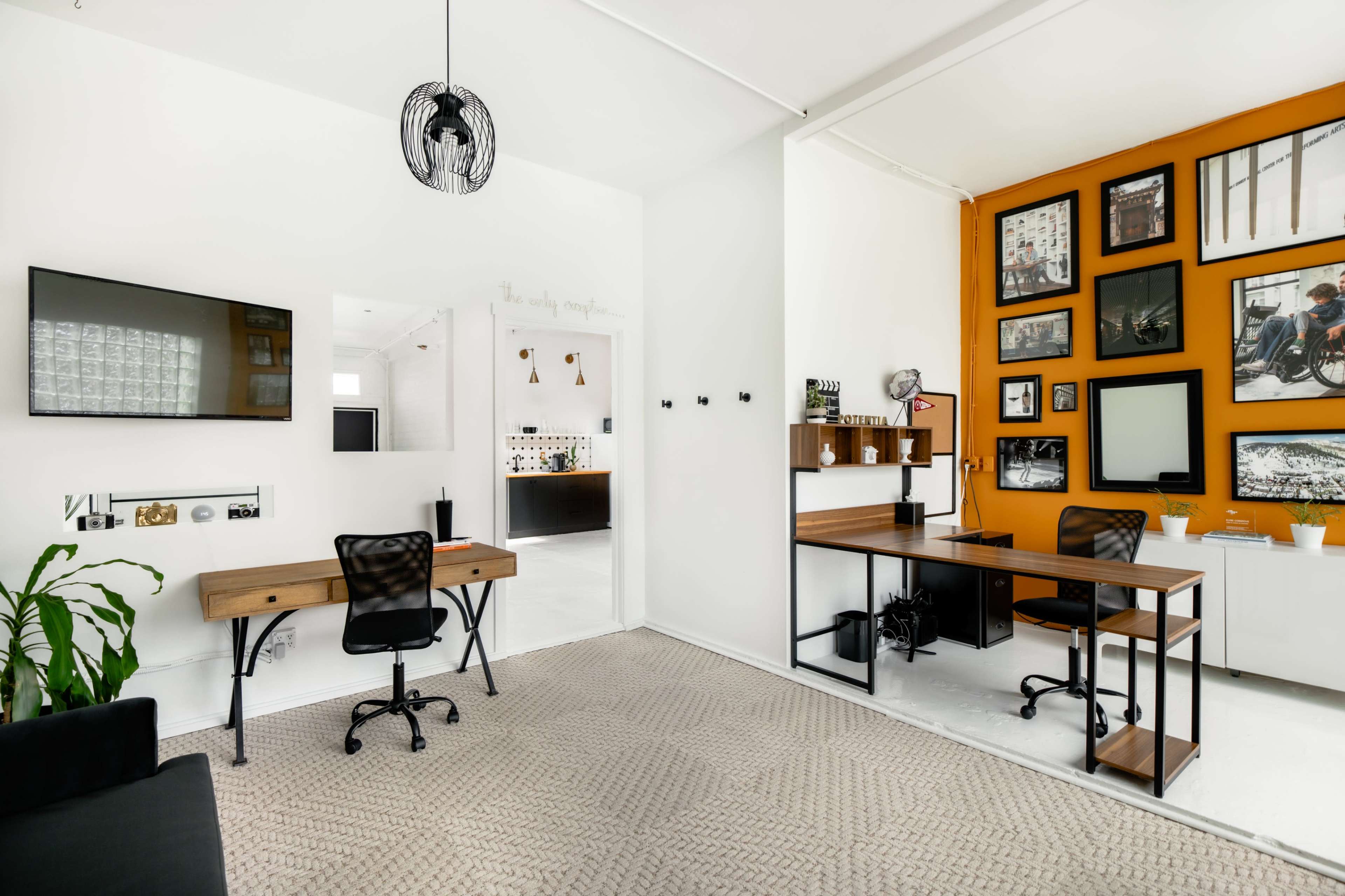A modern office space featuring two workstations, a large wall with framed photographs, and a combination of light and dark décor elements.