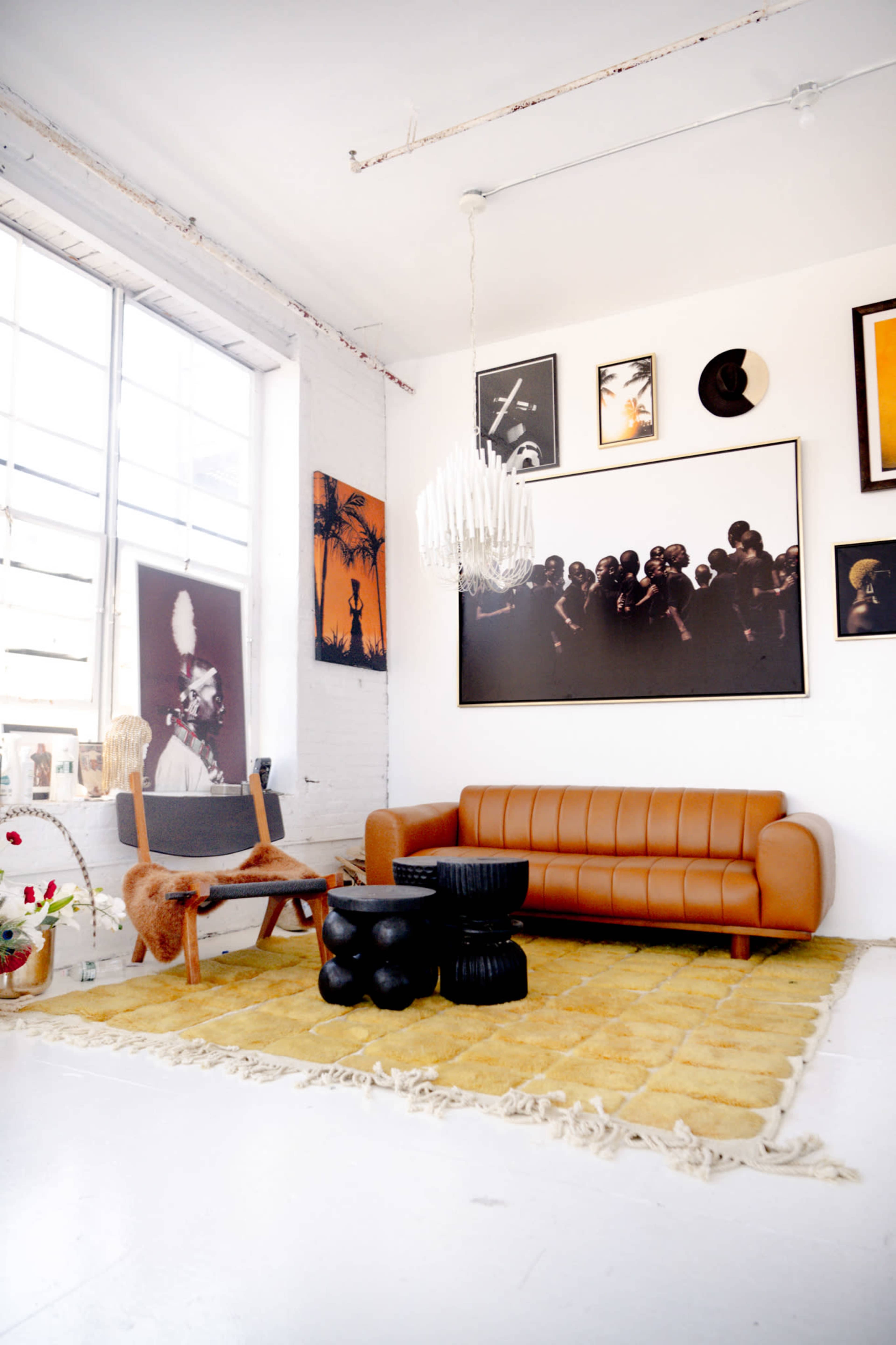 A modern living space featuring a brown leather sofa, a black coffee table, a shaggy yellow rug, and various framed artworks on the white walls.