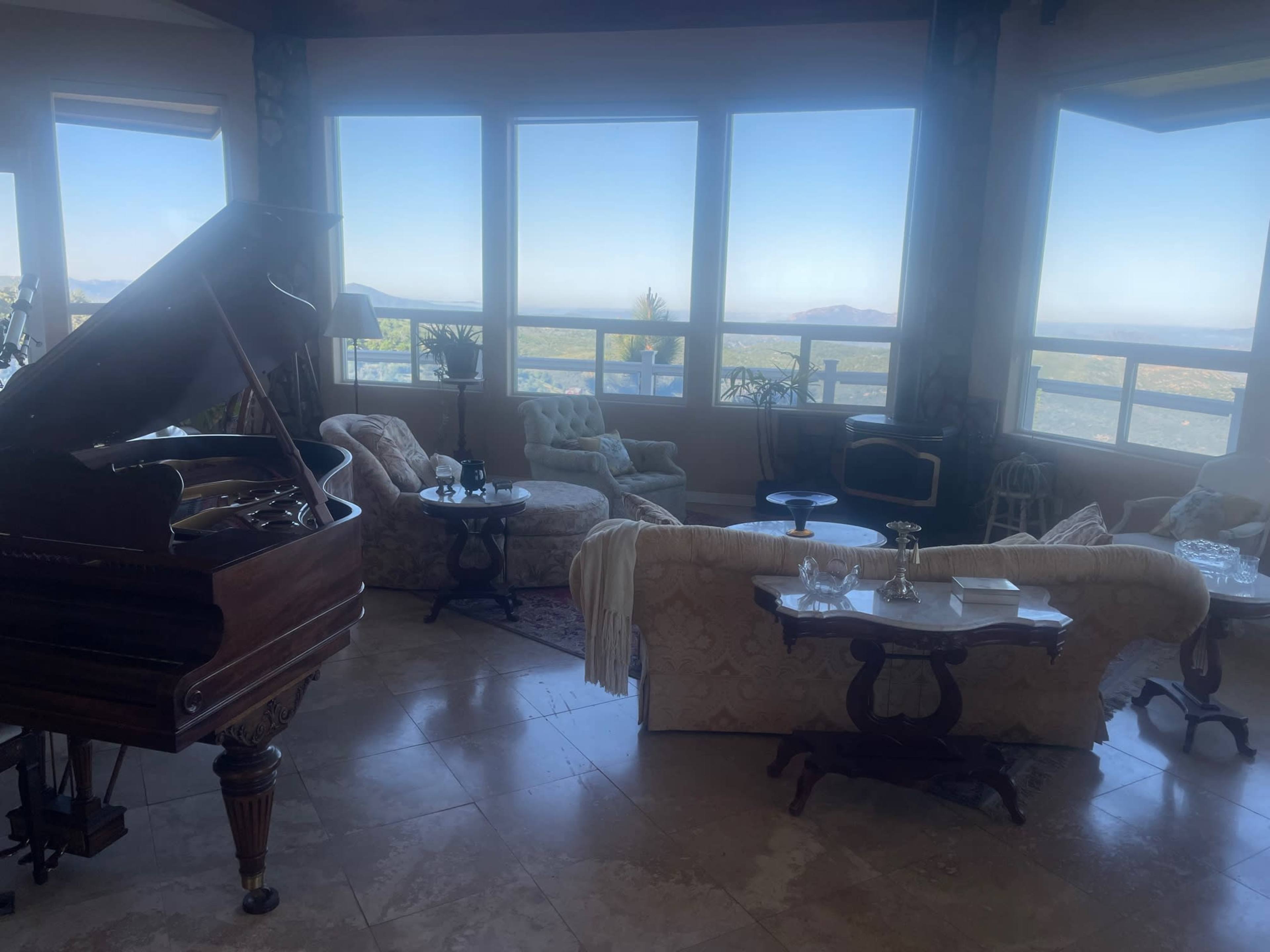 A living room with a grand piano, several seating areas, and large windows offering views of a landscape.