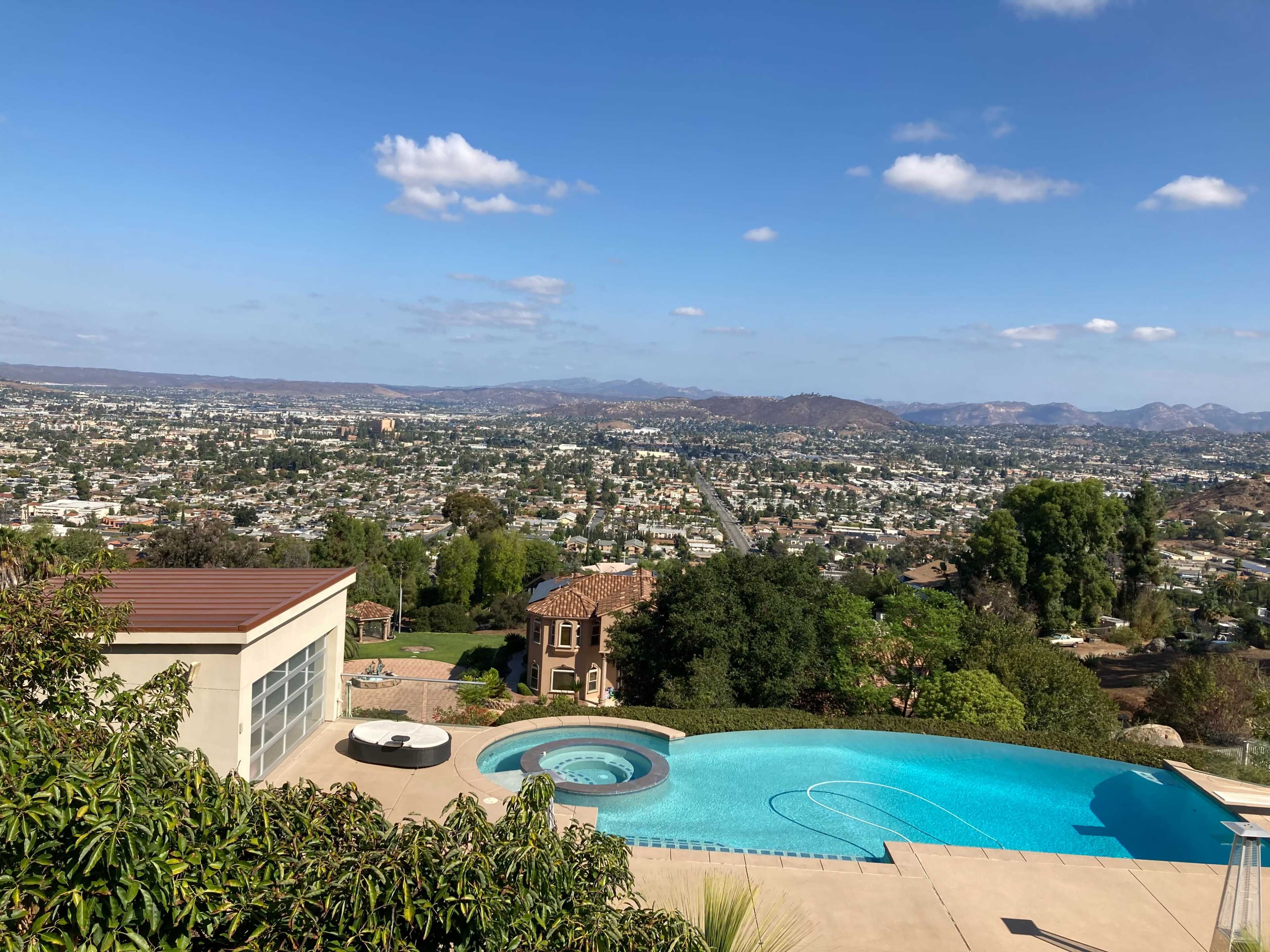 A hillside property with a pool overlooking a valley and distant mountains under a partly cloudy sky.