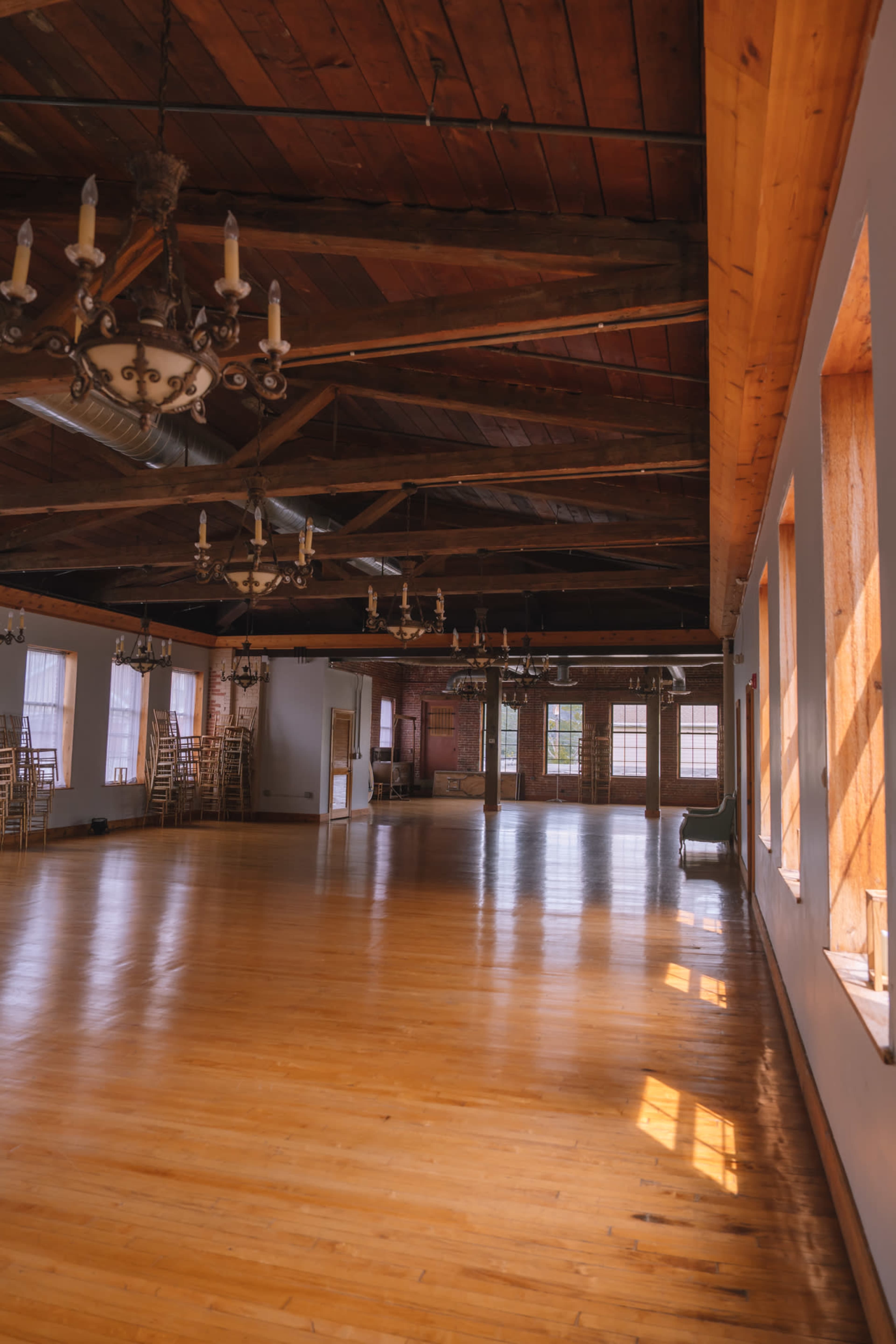 The image shows an empty wooden hall with large windows and exposed wooden beams in the ceiling.