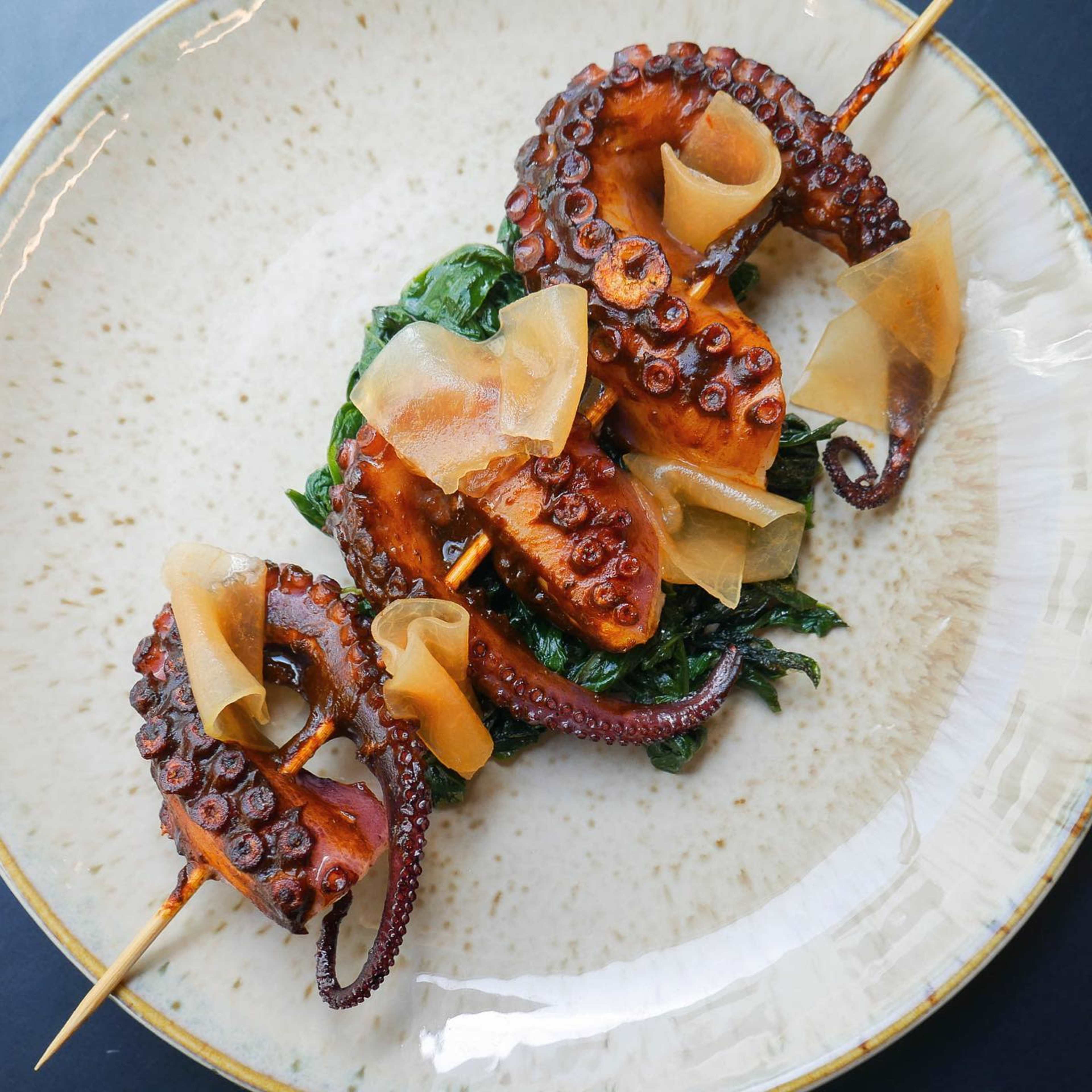 The dish features grilled octopus tentacles served on a bed of sautéed greens with thin slices of pickled vegetables.