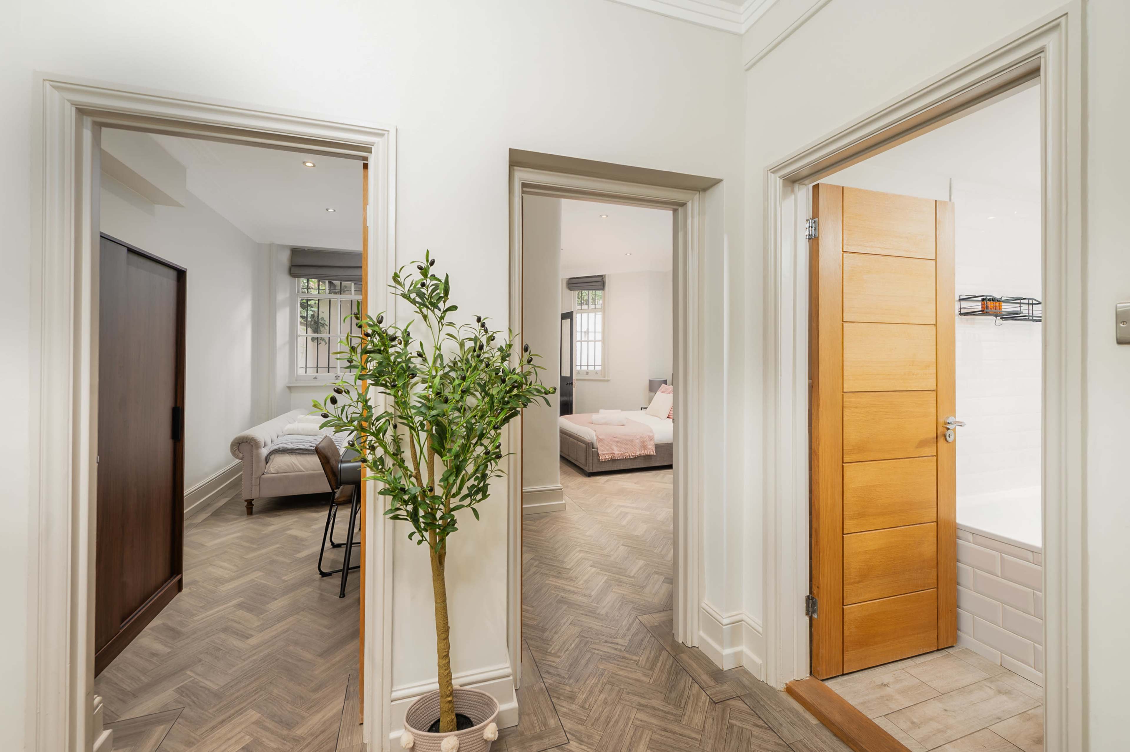 The image shows a hallway with three doorways: one leading to a room with a bed, another to a bathroom, and the third is closed.