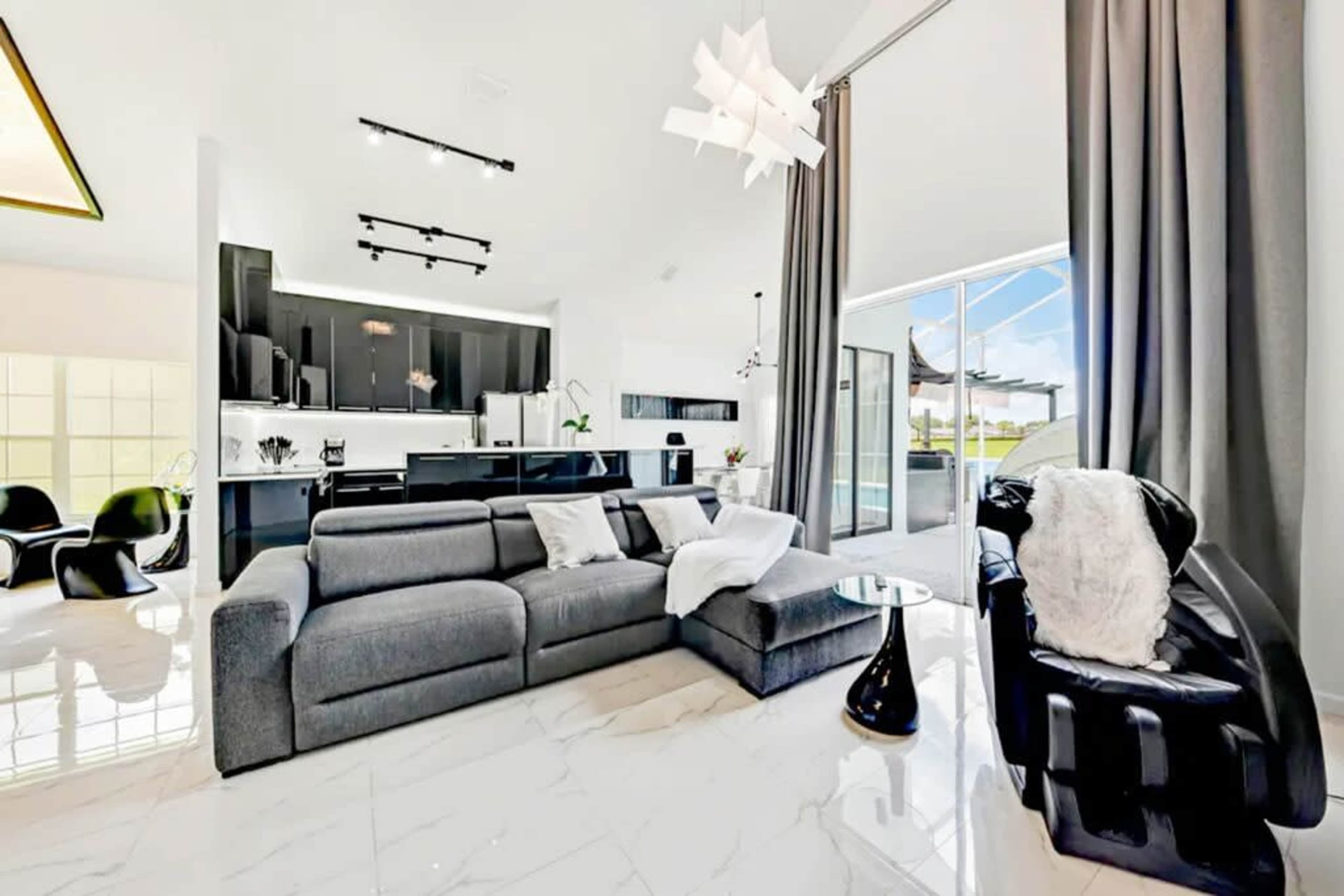 The image shows a modern living room featuring a gray sectional sofa, a black armchair, and large windows that provide natural light.