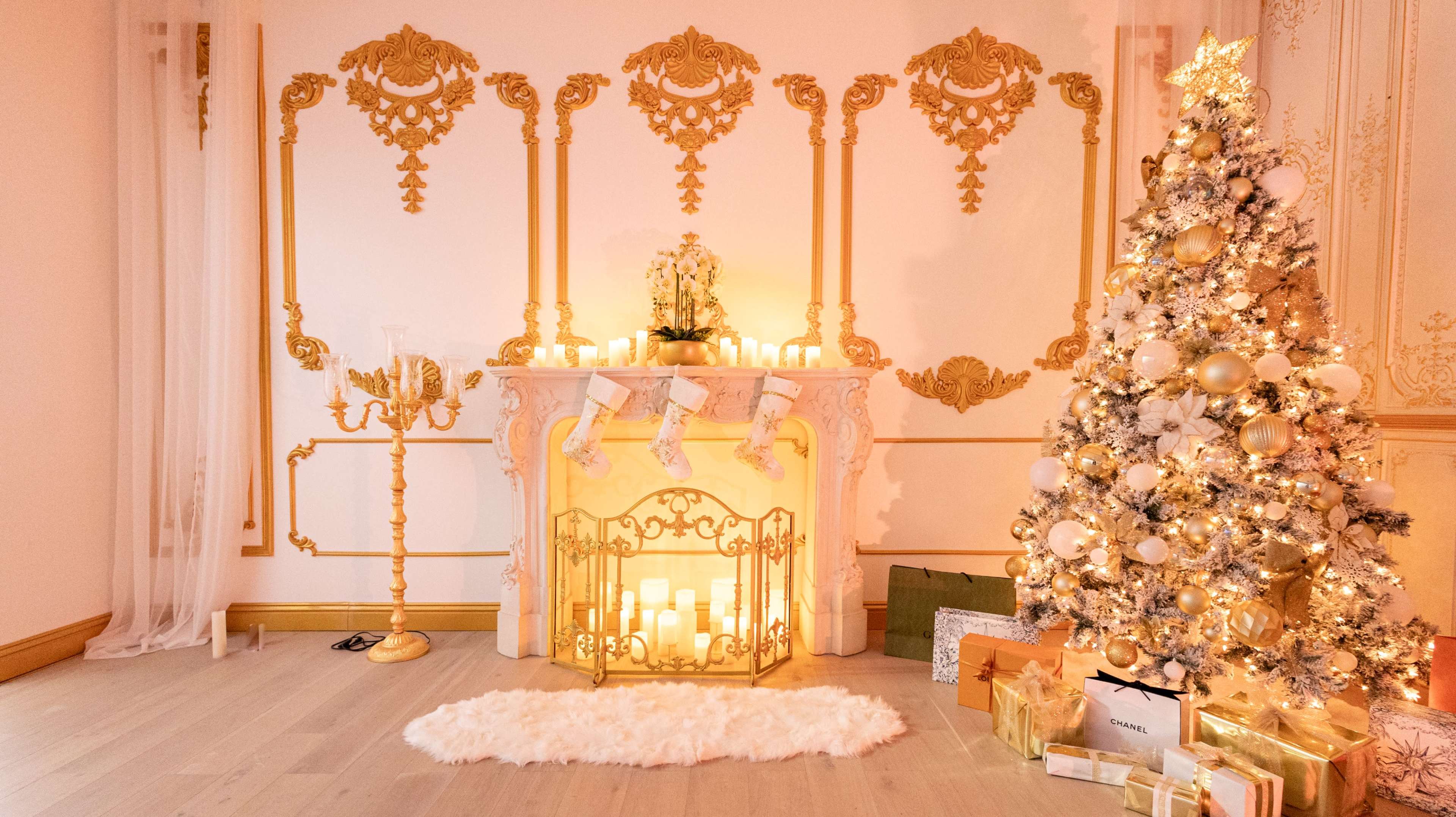 The image shows a decorated room featuring a gold-accented fireplace with candles and a Christmas tree adorned with ornaments and lights.
