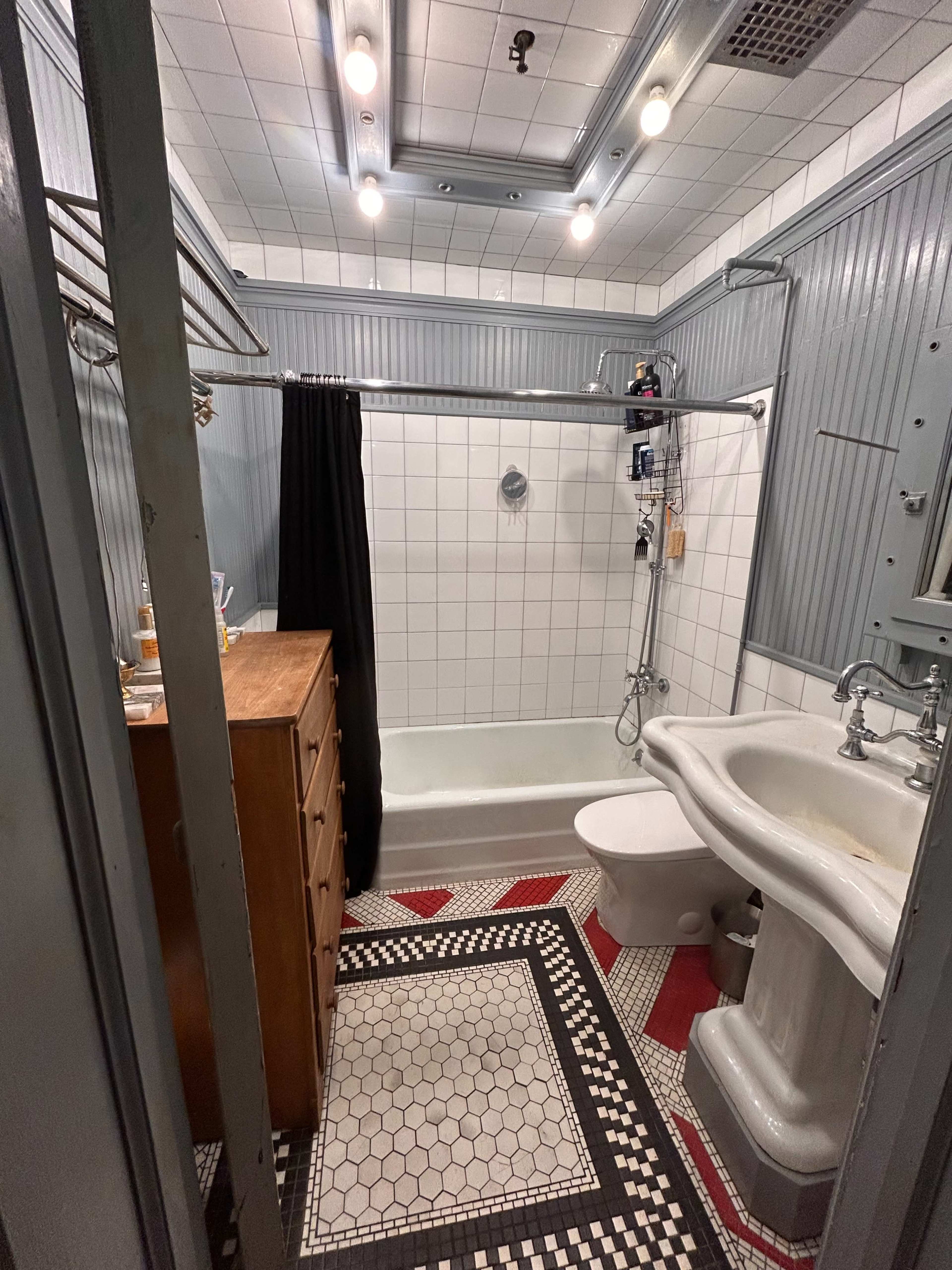 The image shows a vintage-style bathroom featuring a clawfoot bathtub, a pedestal sink, a toilet, and patterned tile flooring.
