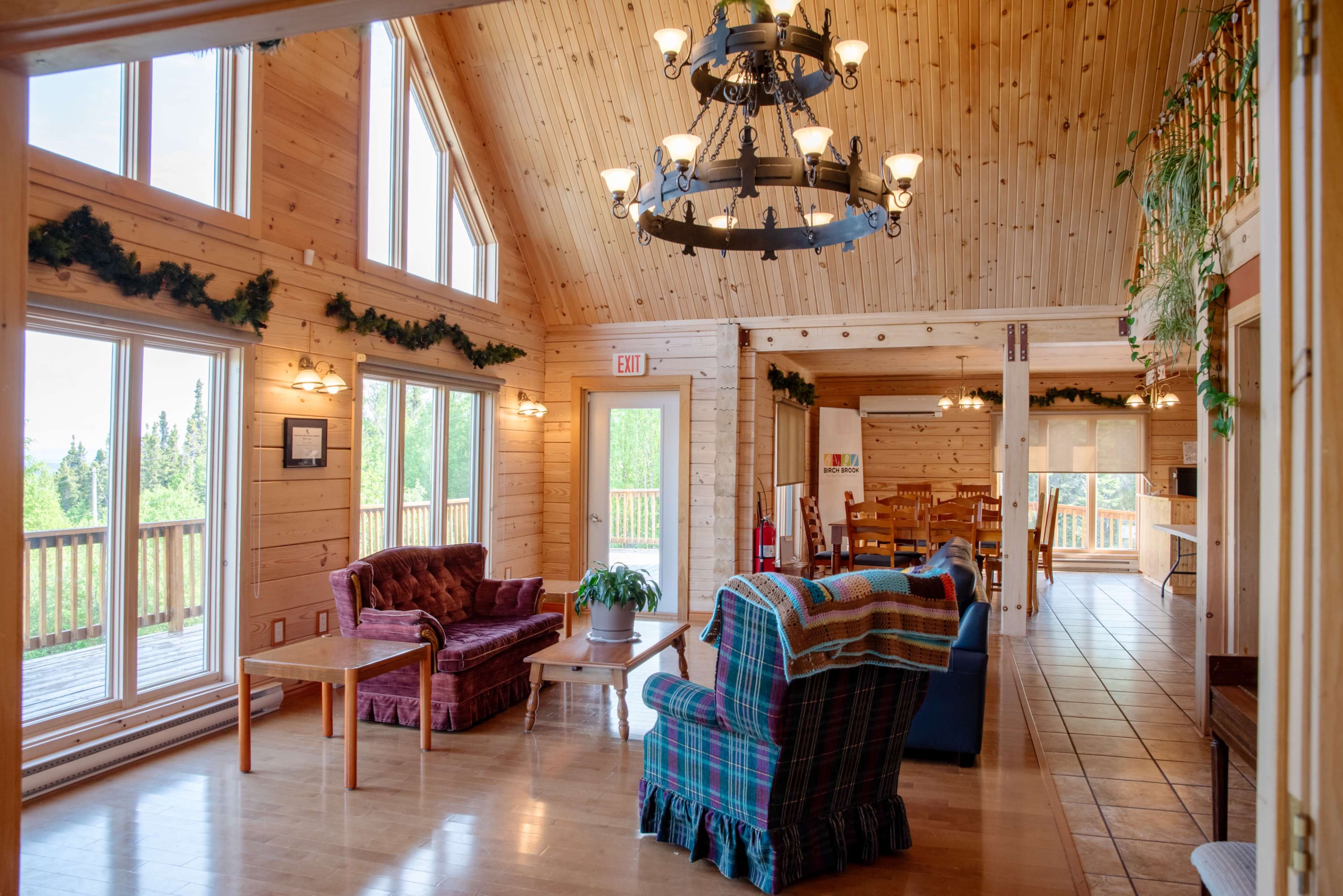 A spacious wooden interior features a seating area with couches and a coffee table, leading to a deck with large windows allowing natural light.