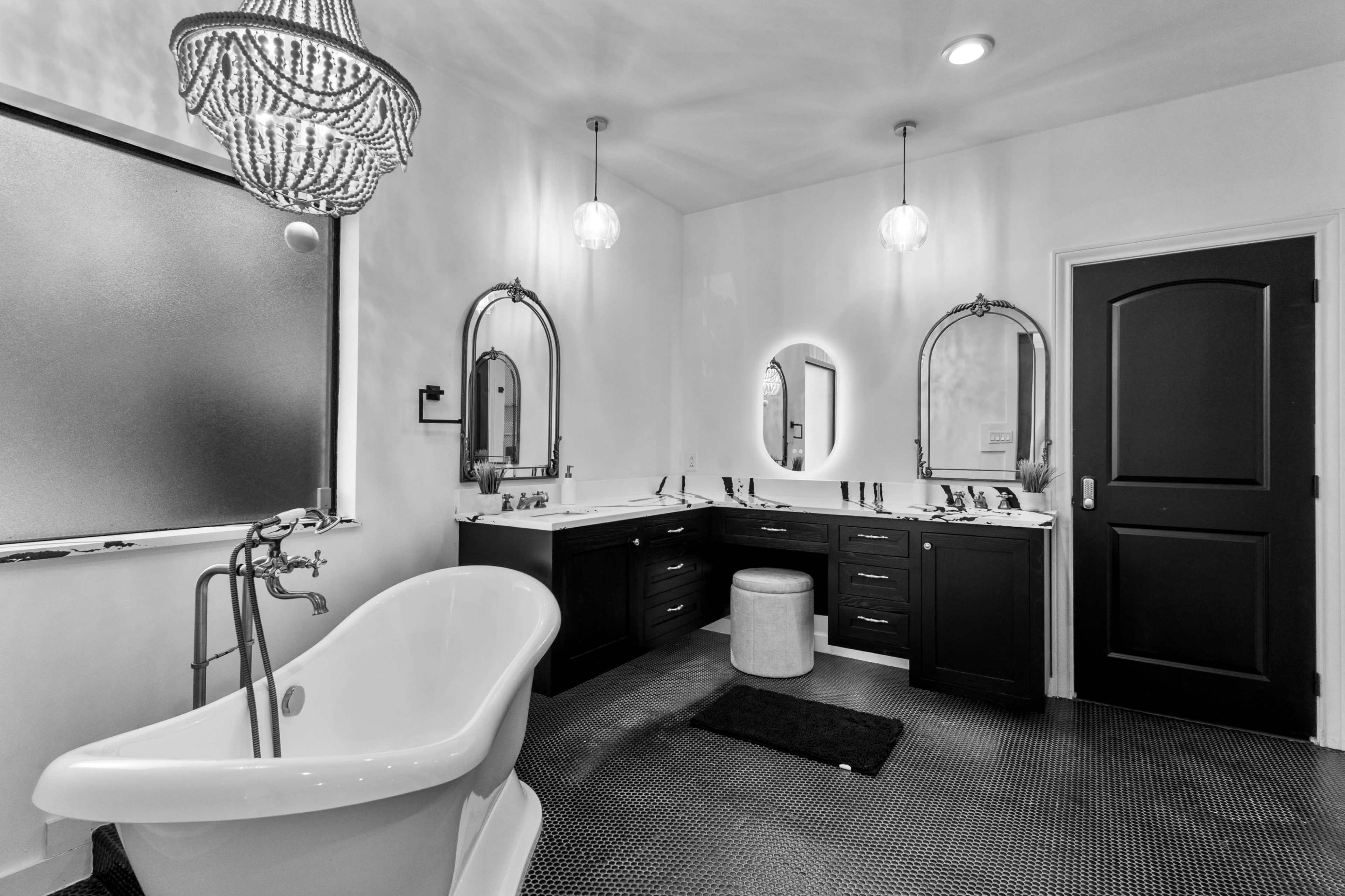 The image shows a spacious bathroom featuring a freestanding bathtub, dual sinks with dark cabinetry, and decorative lighting fixtures.