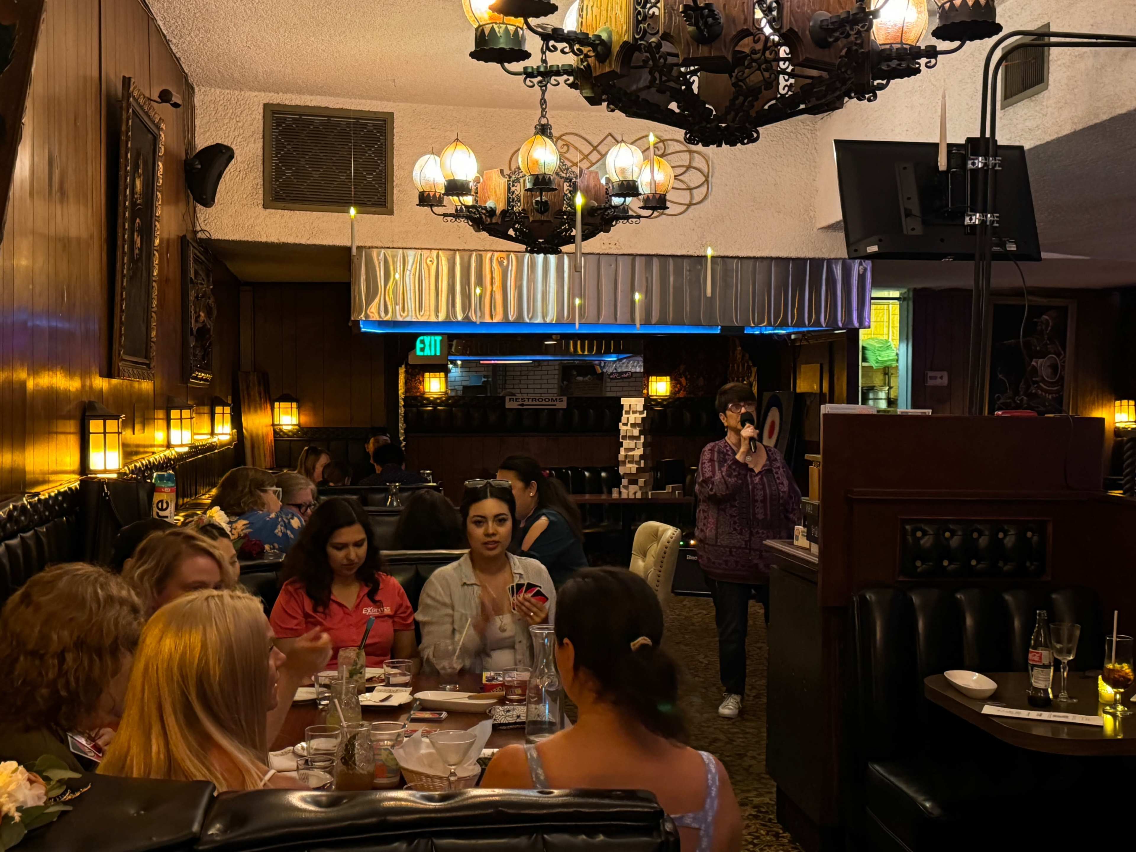 A group of people sits at a large table in a restaurant, while a staff member is seen walking nearby.