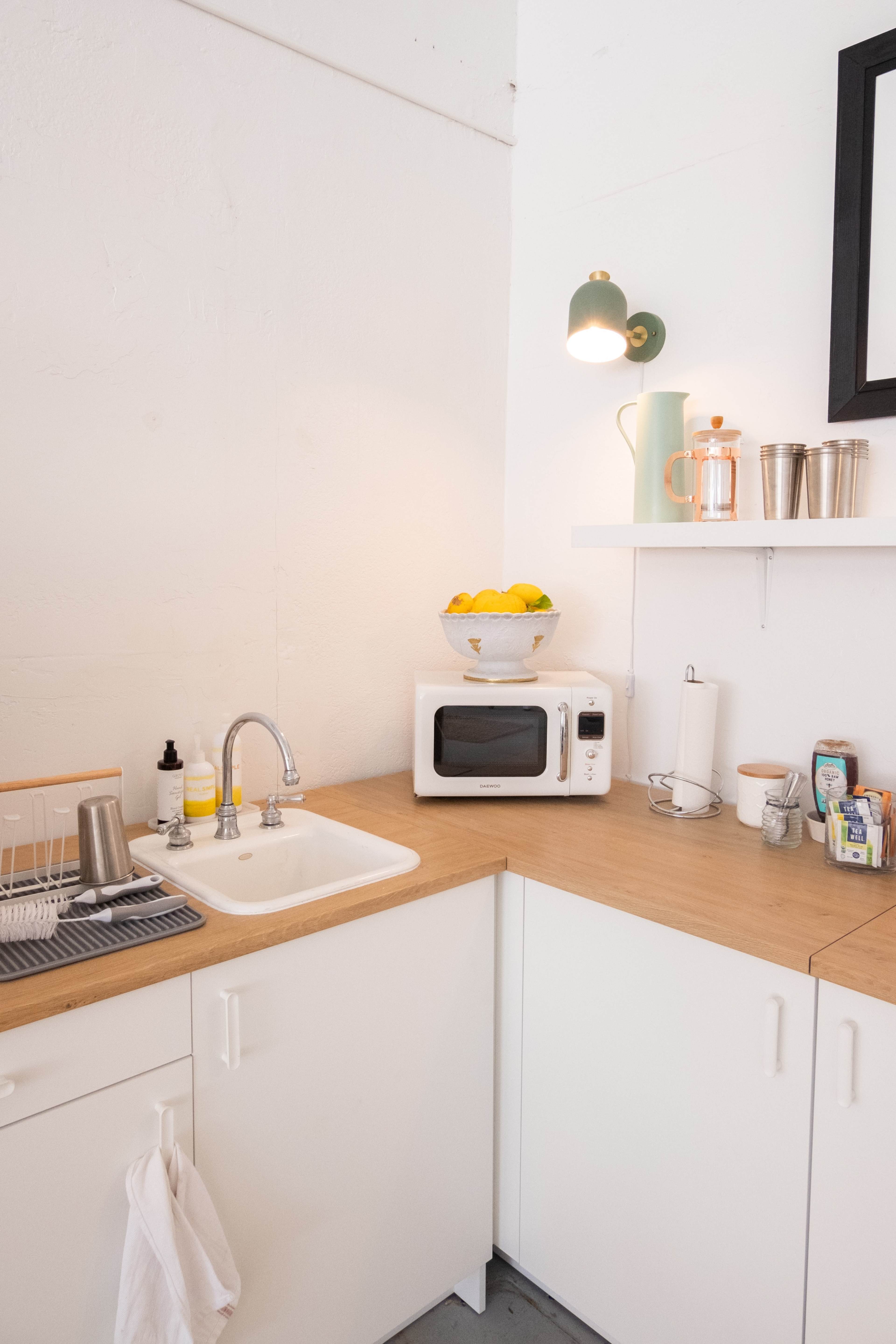 A corner kitchen with a sink, a microwave, a bowl of lemons on a shelf, and organized kitchen supplies.