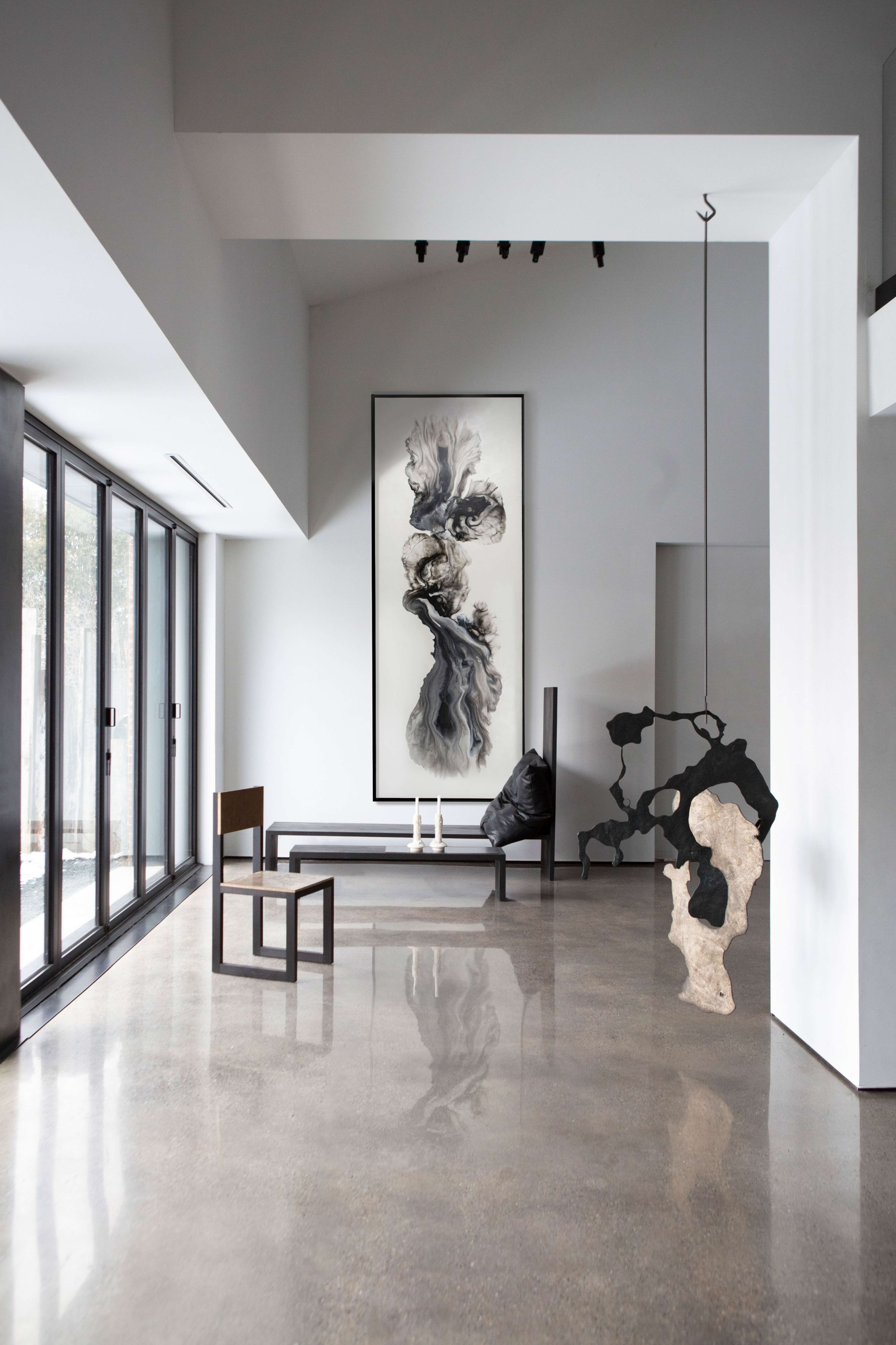 The interior space features a minimalist design with large windows, a gray color palette, and contemporary art pieces against polished concrete floors.