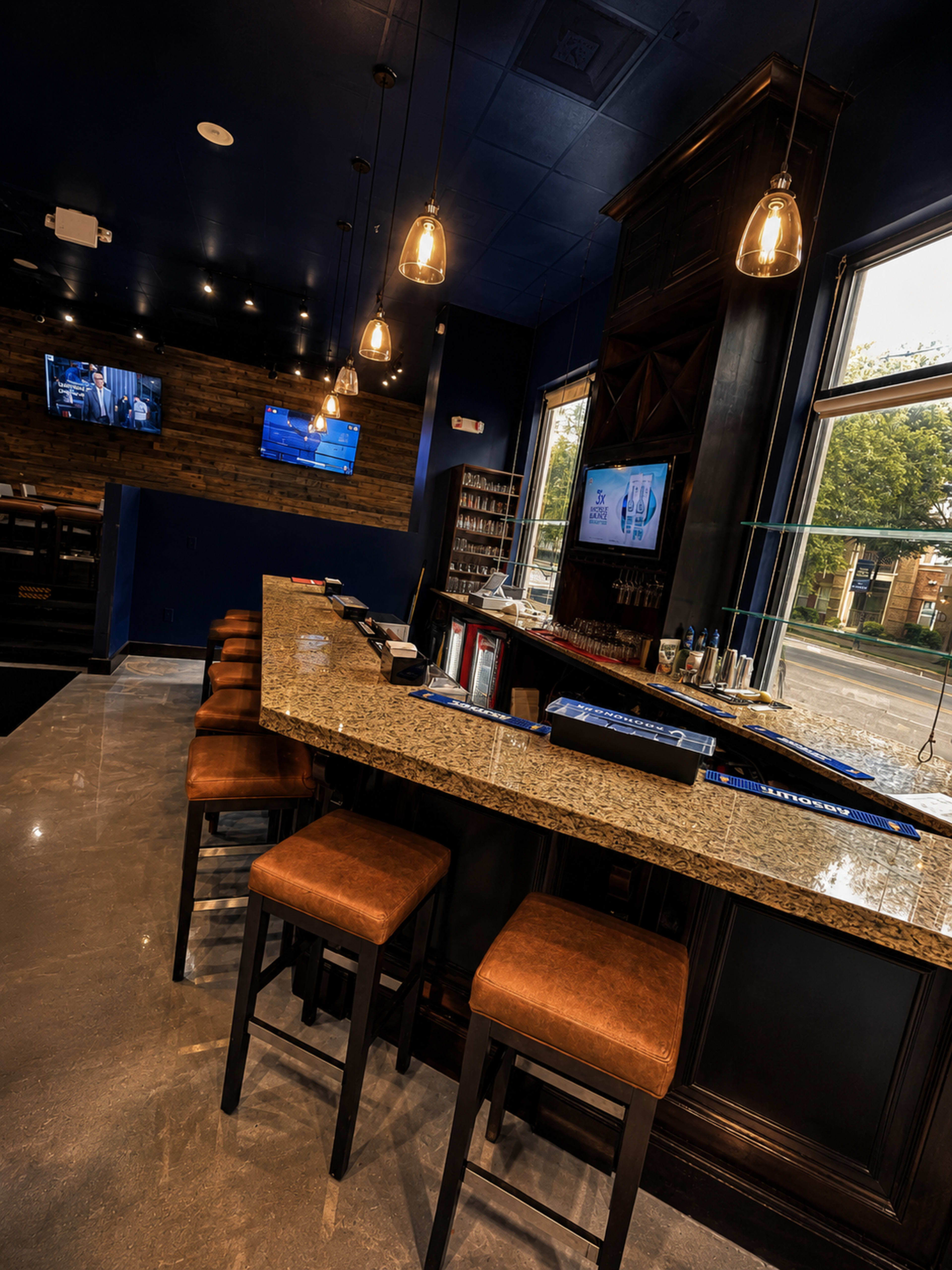 The image shows a modern bar interior with a granite countertop, wooden accents, and several bar stools arranged in front of it.