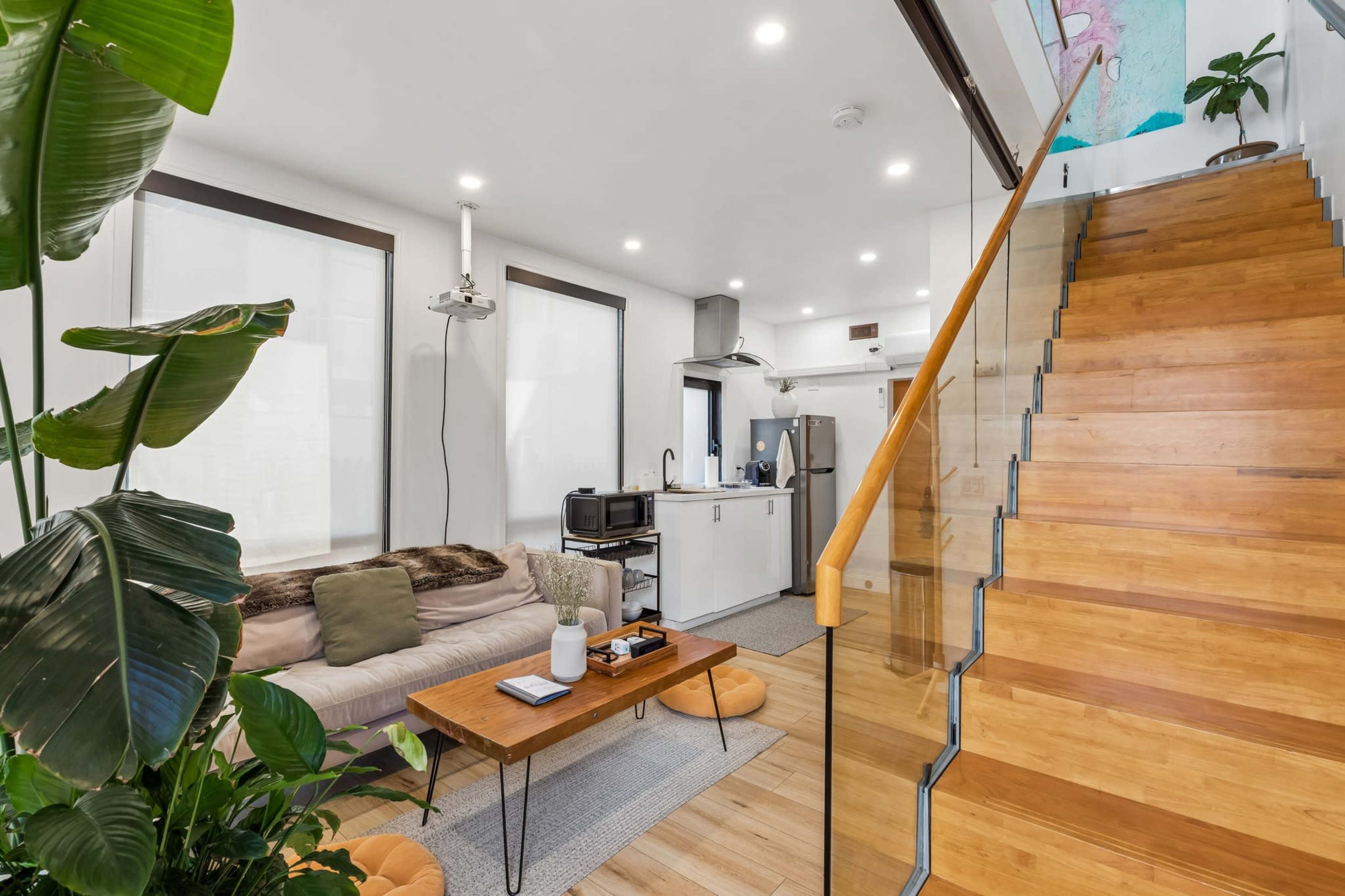 The image shows a modern living space with a staircase, a couch, a coffee table, and a kitchen area visible in the background.