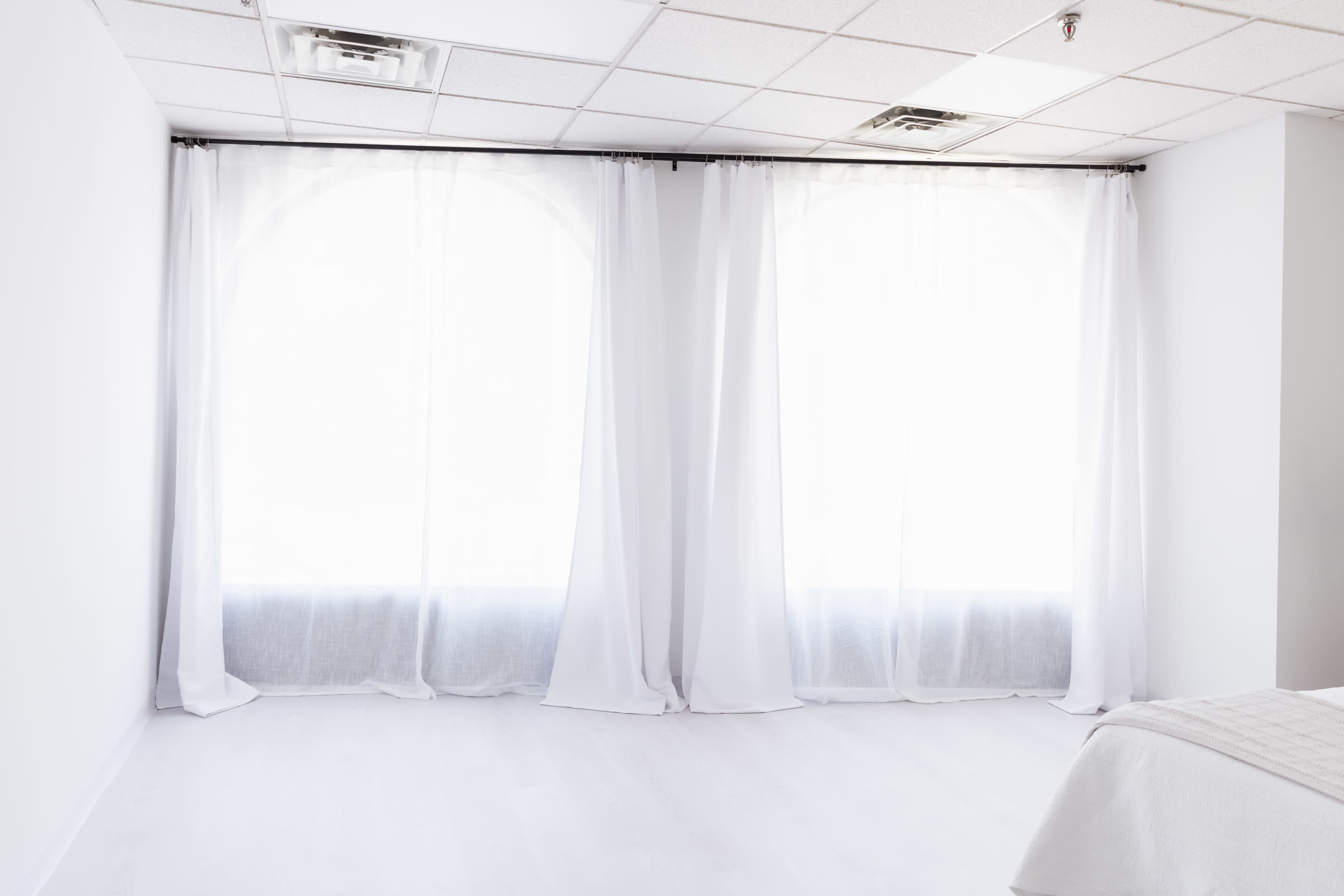The image shows a bright, minimalist room with large windows covered by sheer white curtains.