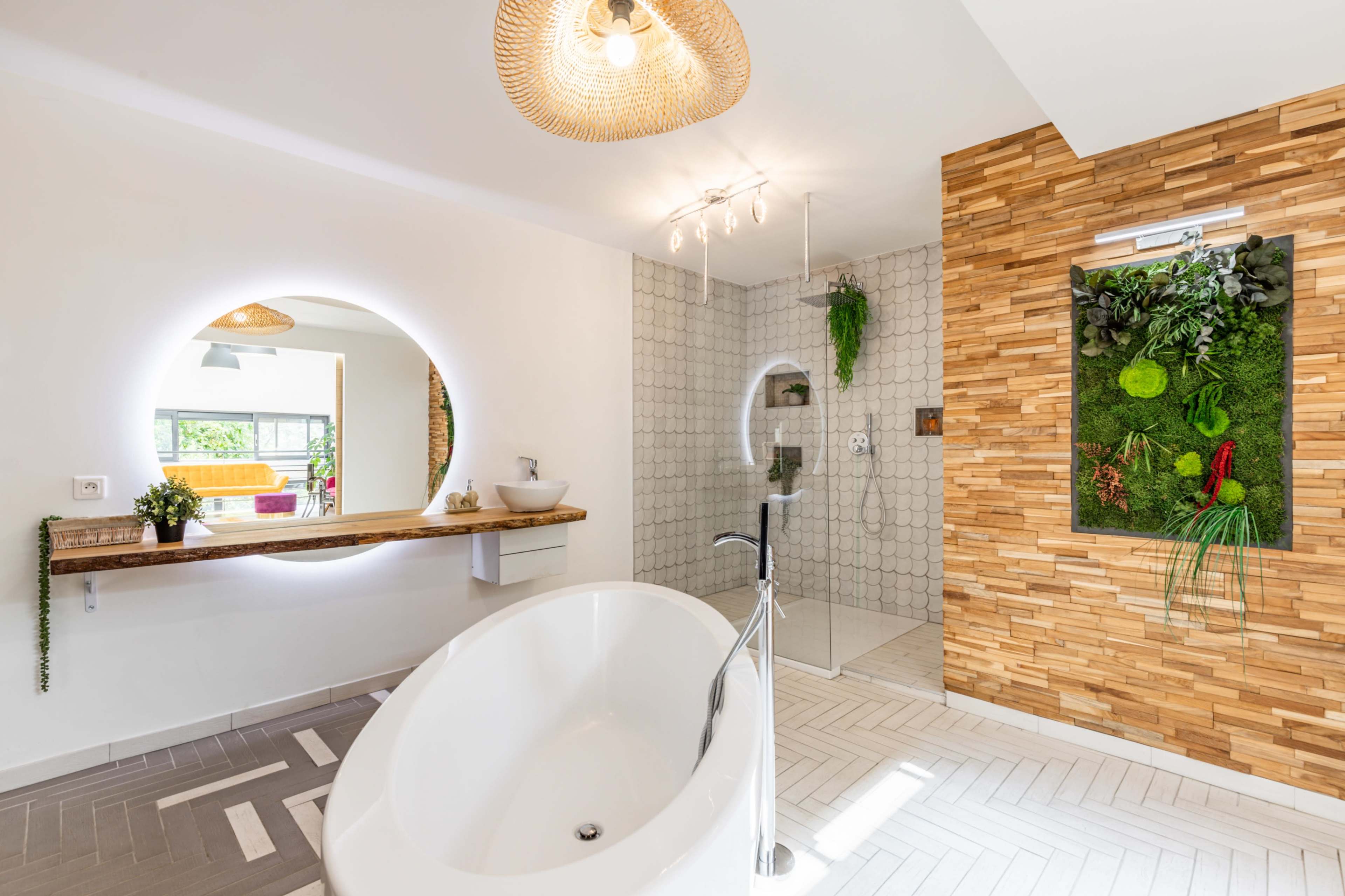 A modern bathroom featuring a freestanding tub, a circular mirror, a walk-in shower, and a vertical garden on a wooden accent wall.