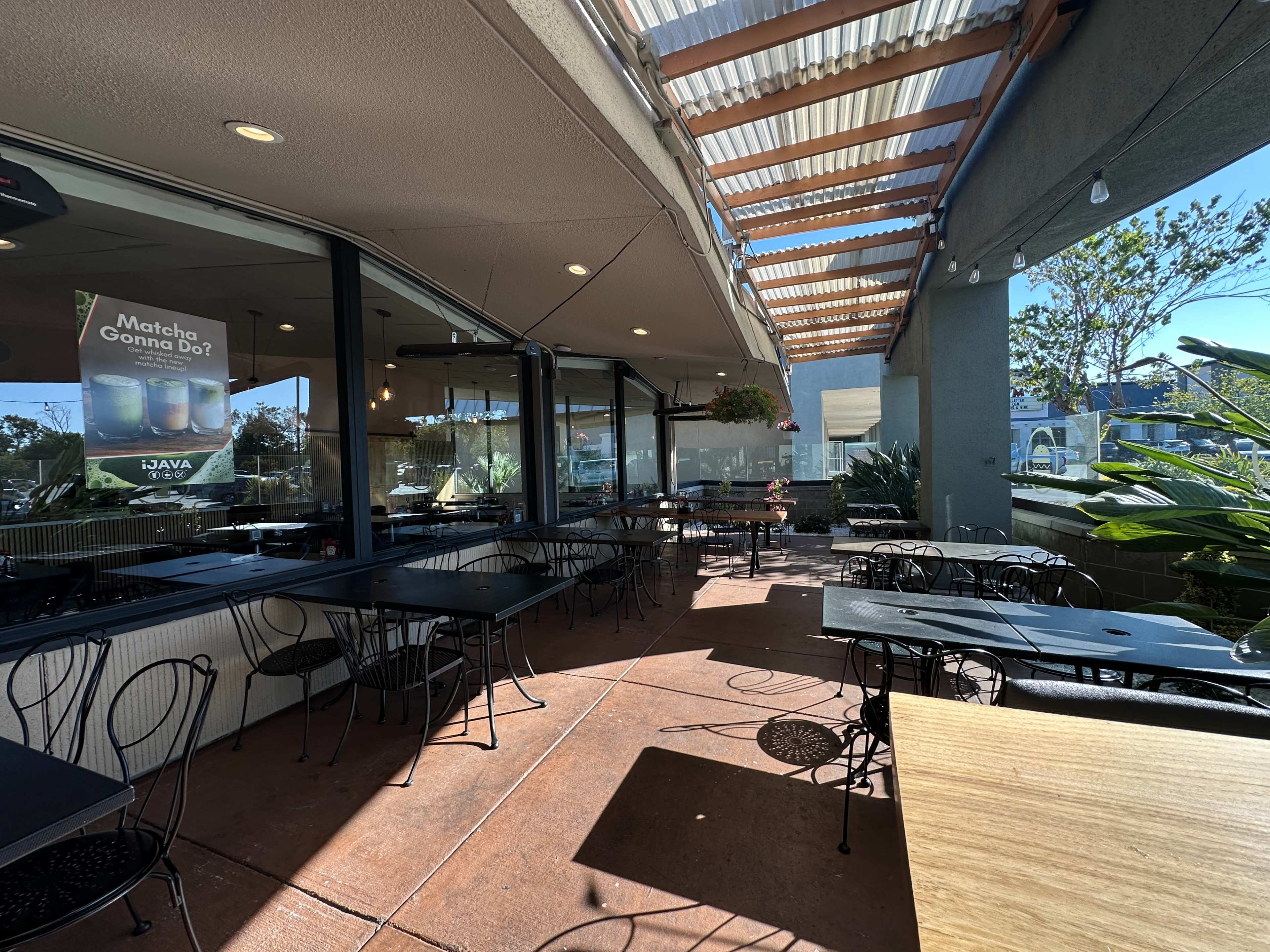 The image shows an outdoor seating area of a café with empty tables and chairs under a covered patio.