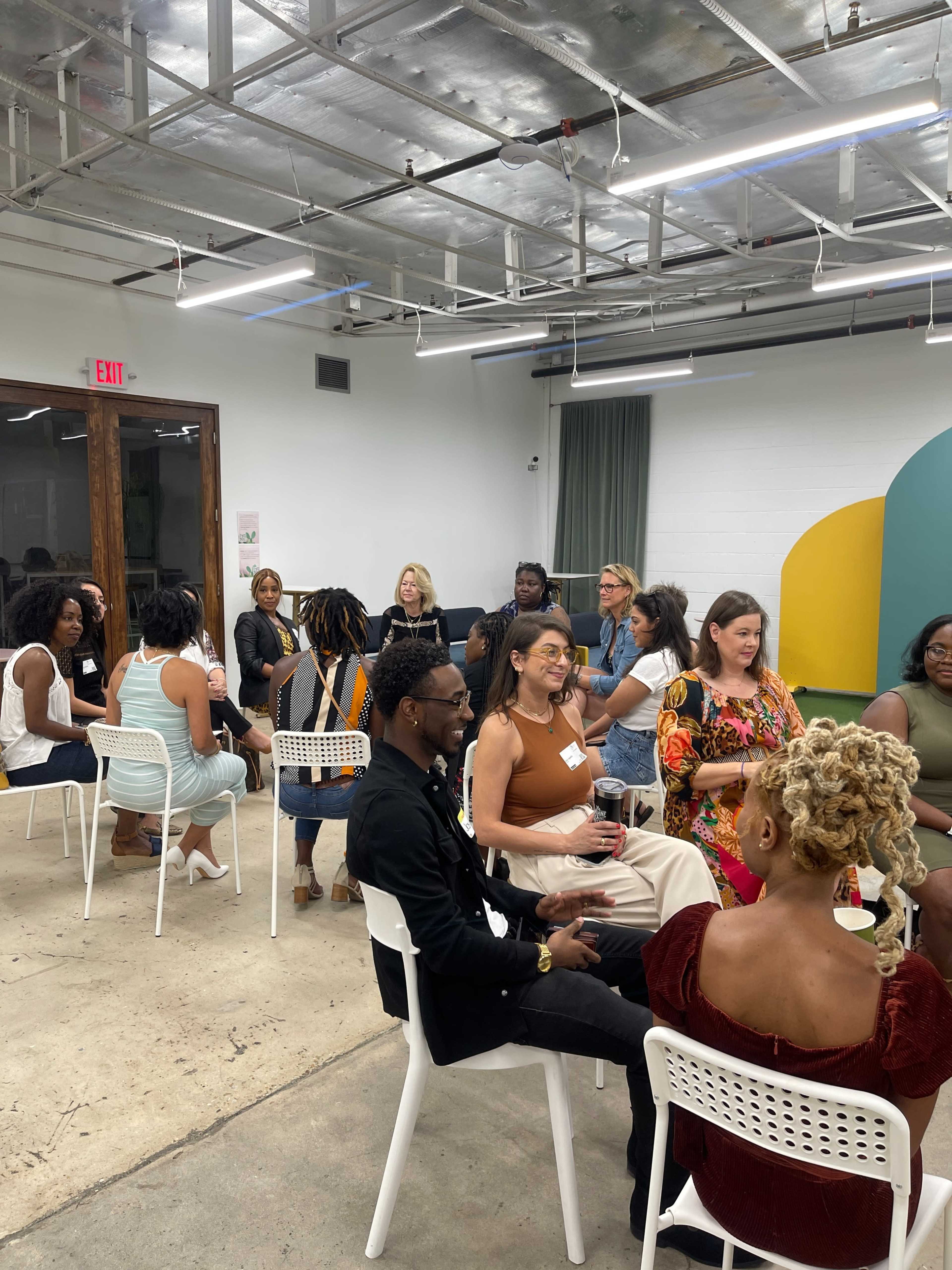 A group of diverse individuals is engaged in conversation while seated in a modern, brightly lit room.