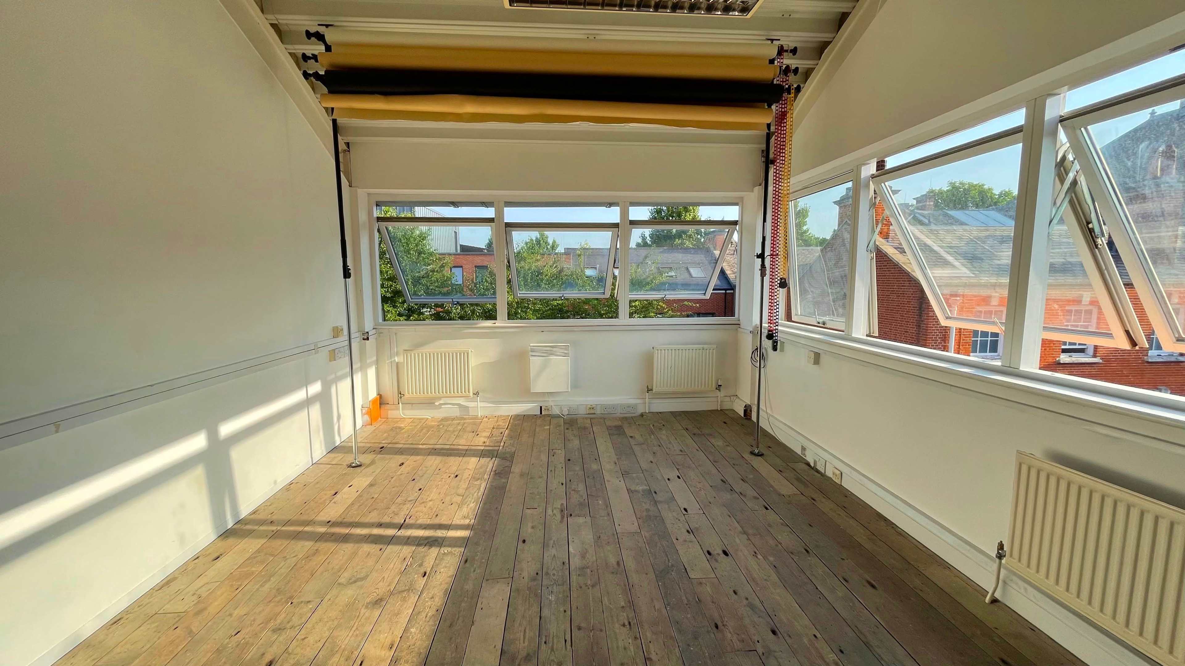 An empty room with wooden floors and large windows that let in natural light.