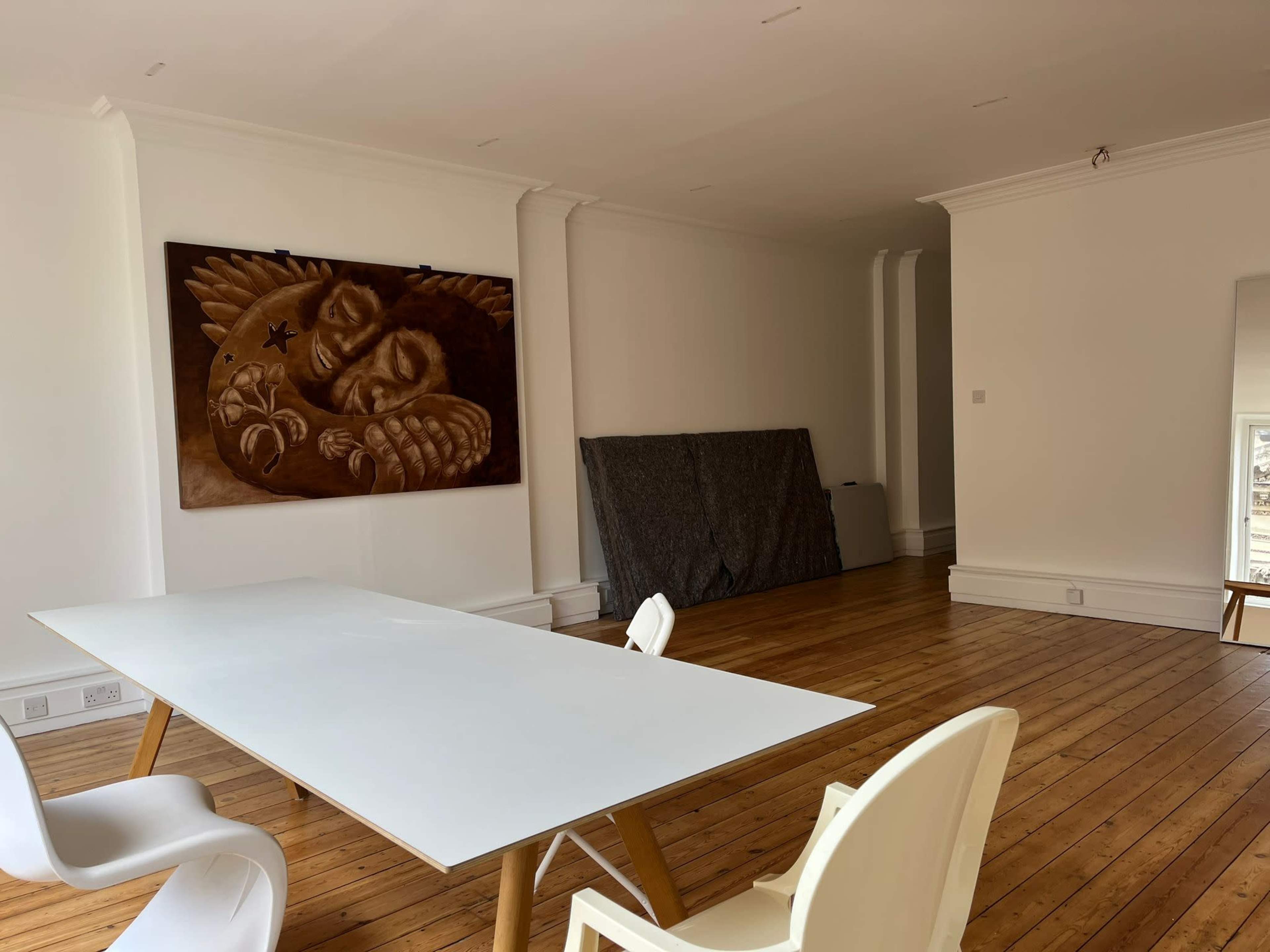 A spacious room features a white table with wooden legs, surrounded by modern chairs, and a large artwork hangs on the wall.