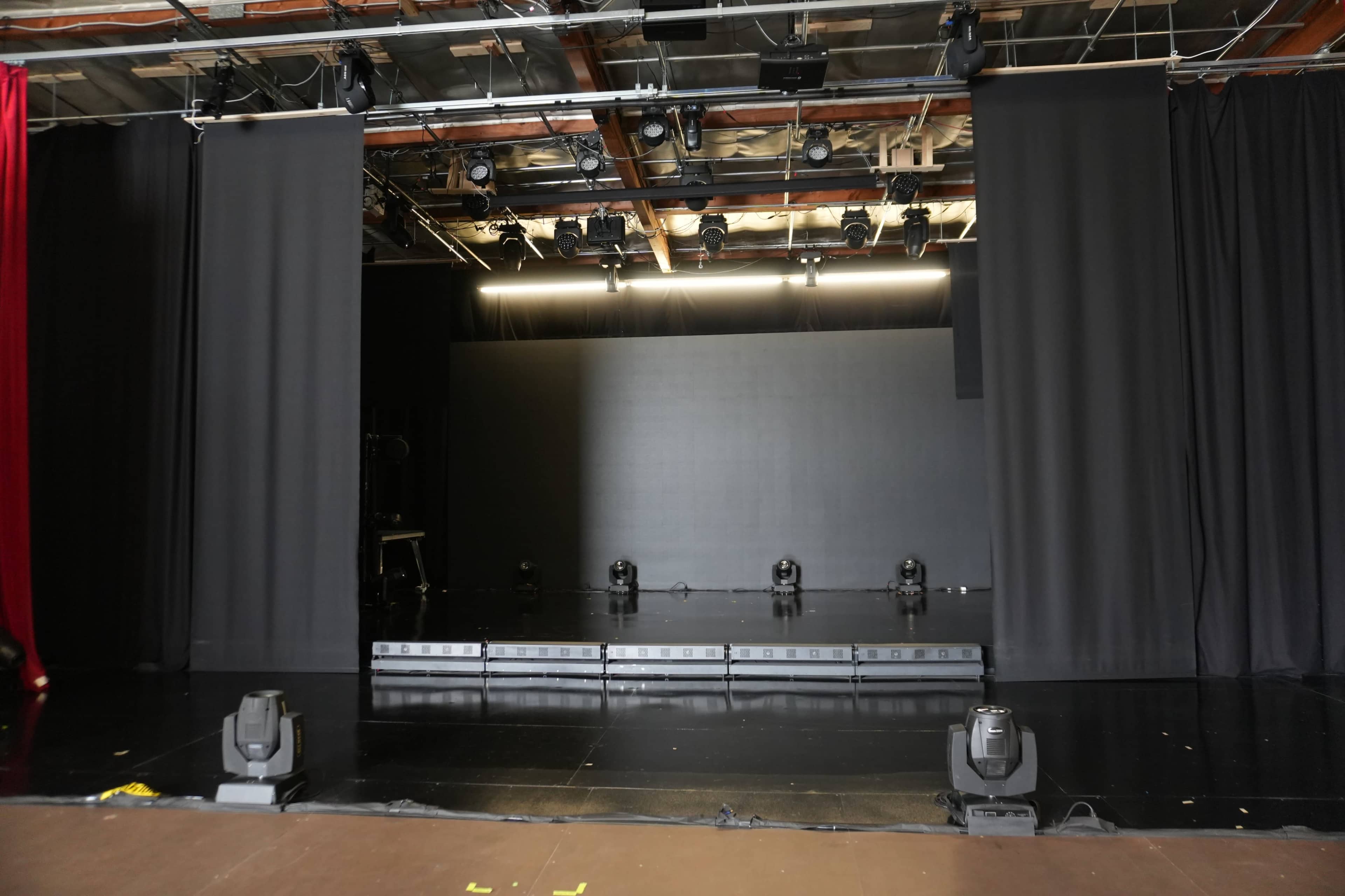 The image shows a stage with a black curtain backdrop, a raised platform, and several stage lights arranged along the front.