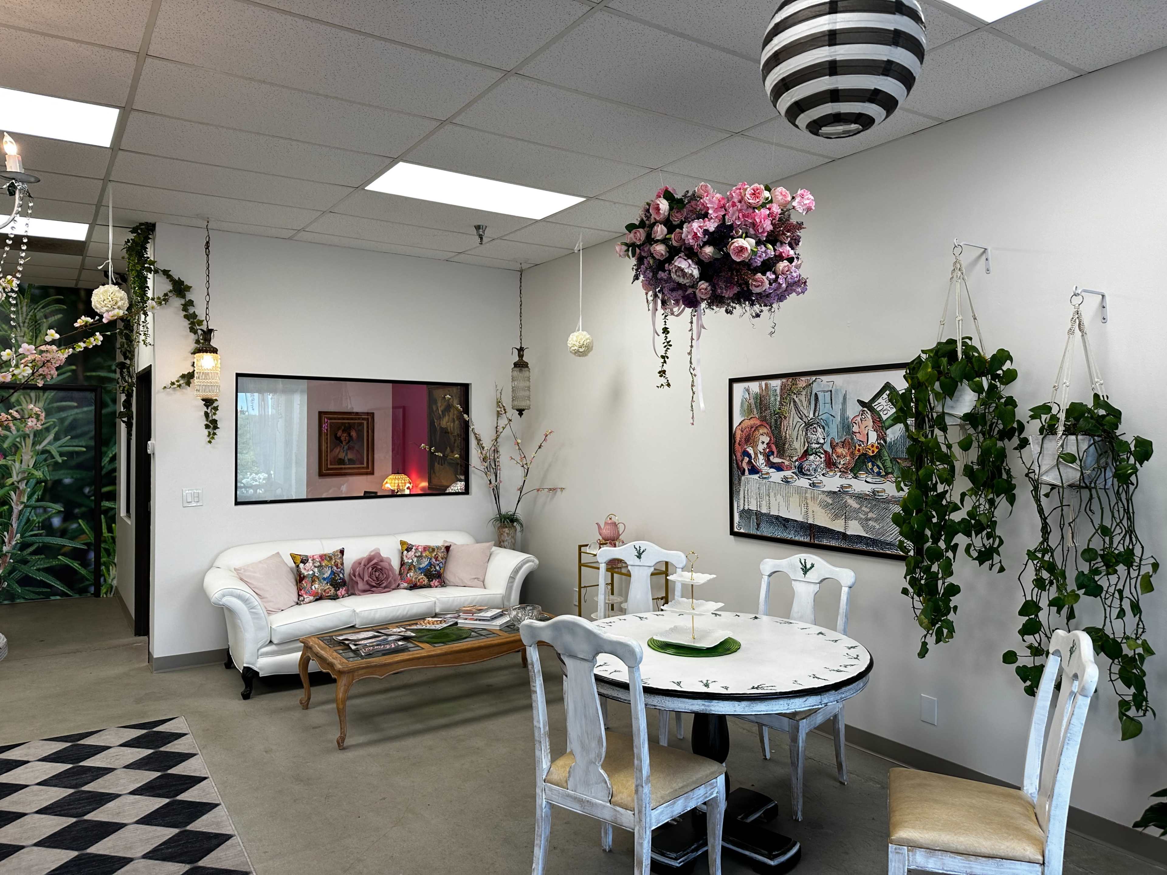 A brightly lit room with a white sofa, a round dining table, and hanging floral decorations.