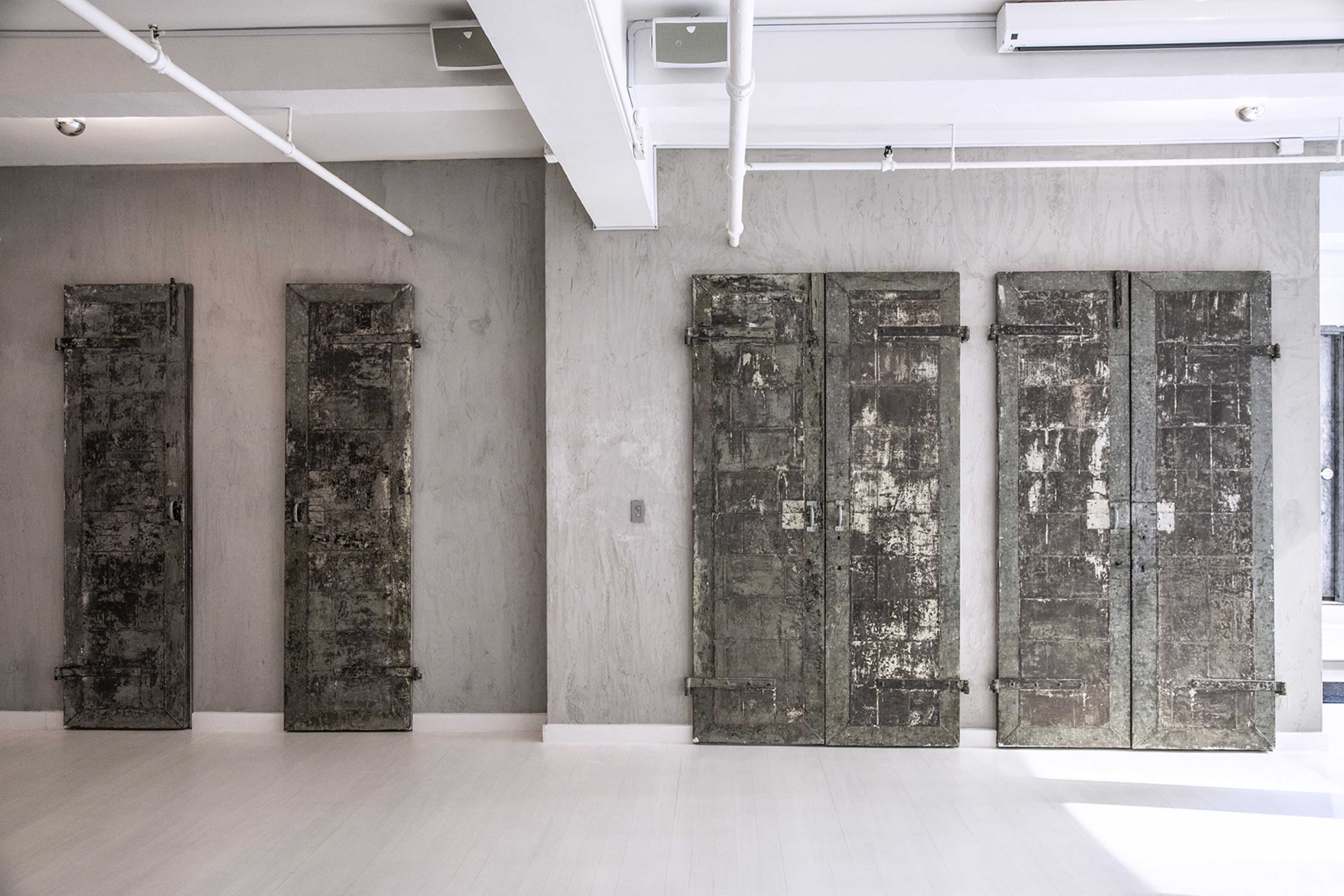 A minimalist interior space featuring four weathered metal doors mounted against a light gray wall.