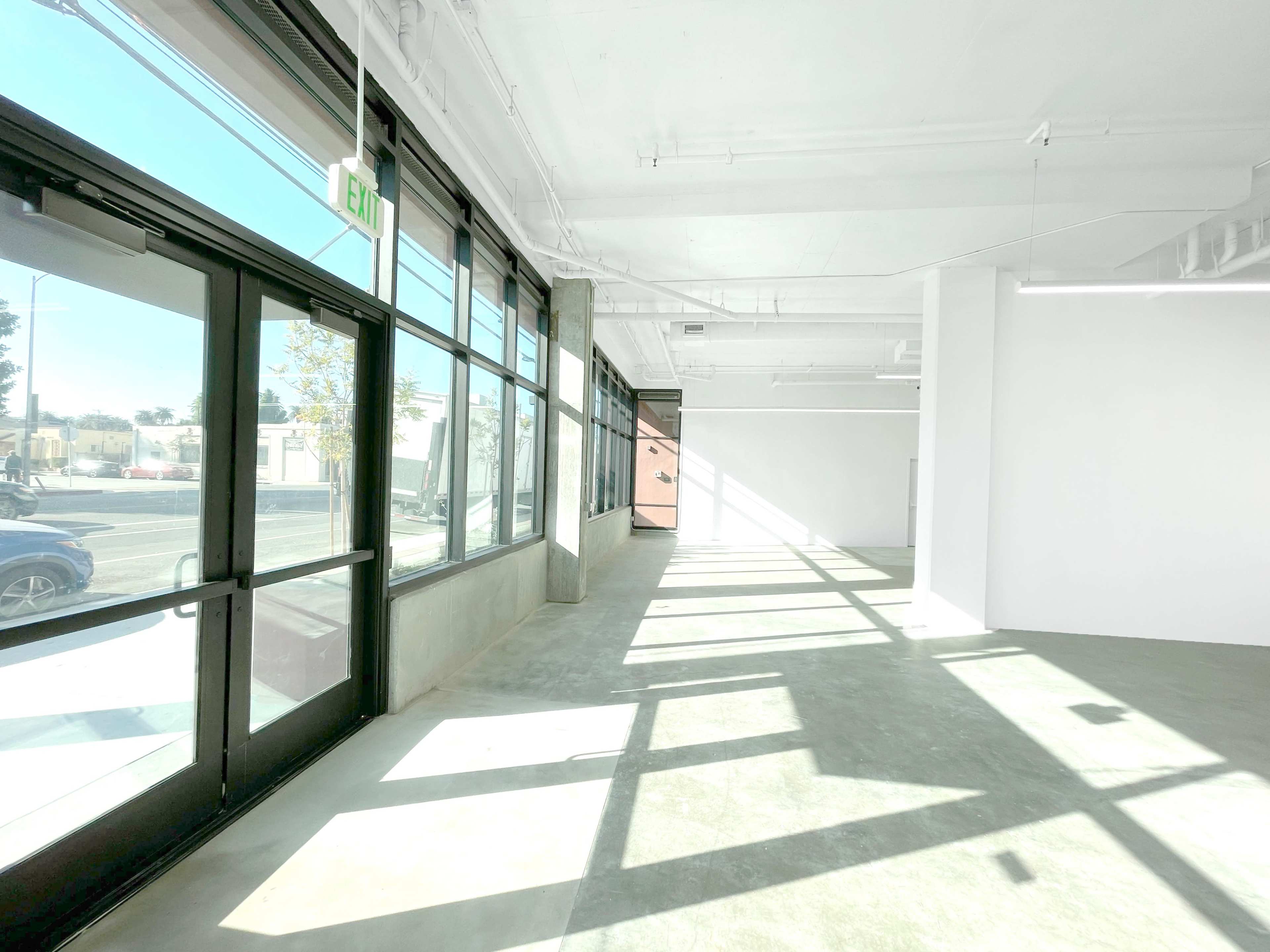 The image shows a spacious, empty room with large windows allowing natural light to fill the space.