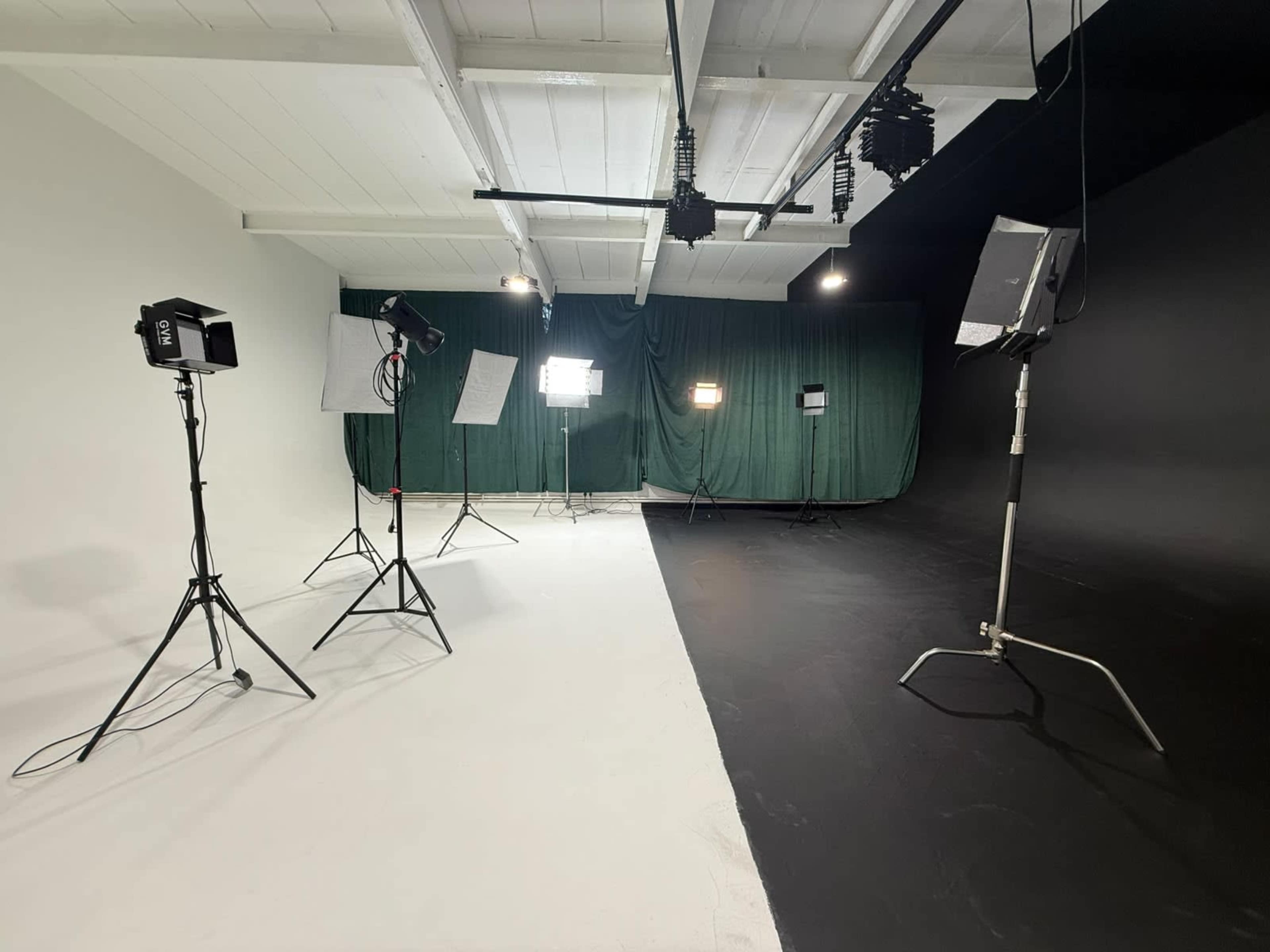 The image shows a photography studio divided into two sections, one with a white backdrop and the other with a black backdrop, equipped with various lighting setups.